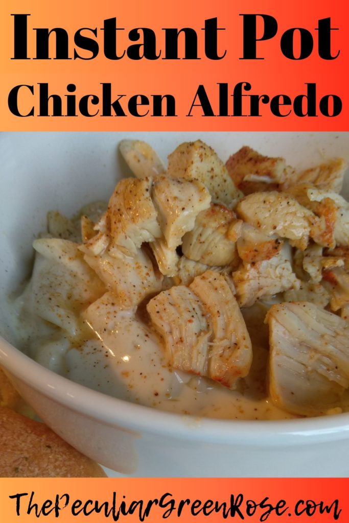 A white bowl filled with chicken alfredo and pasta with a breadstick on the side.