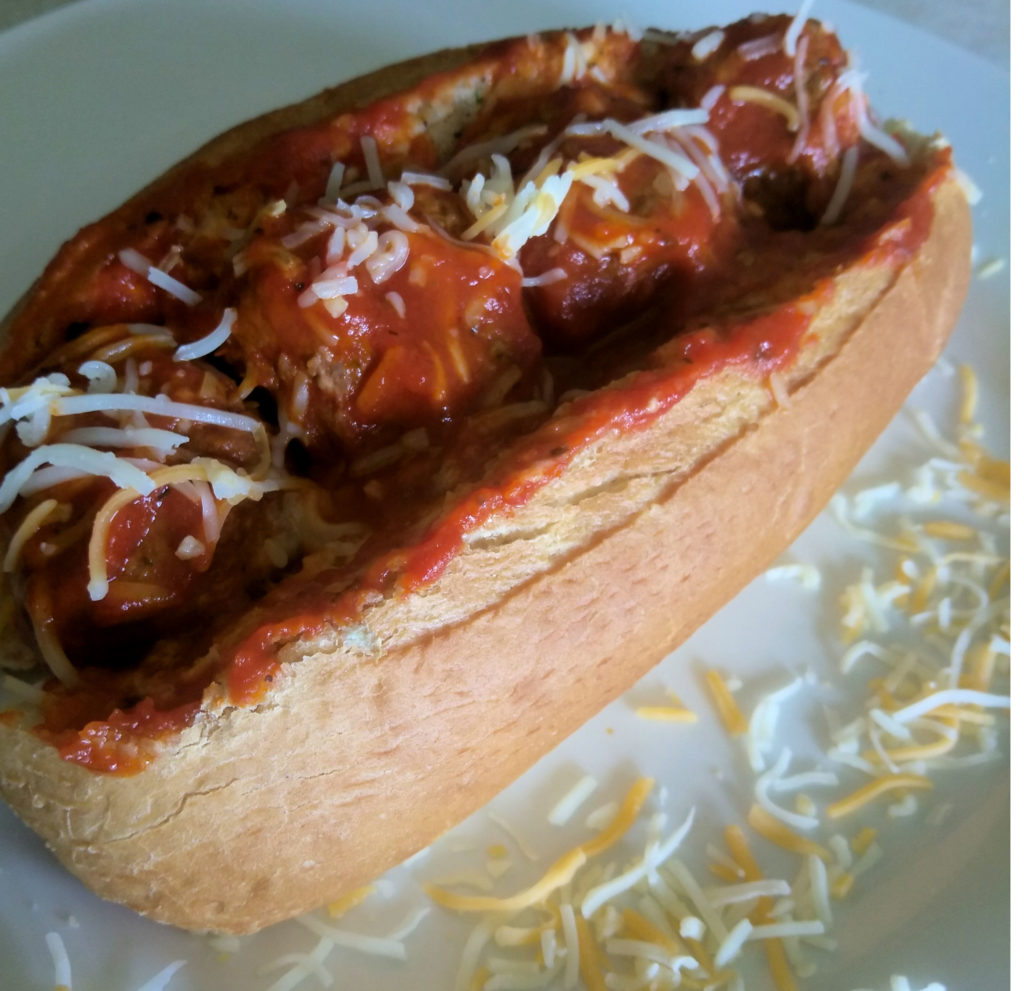 White plate sprinkled with shredded cheese with a meatball and marinara sub in the middle