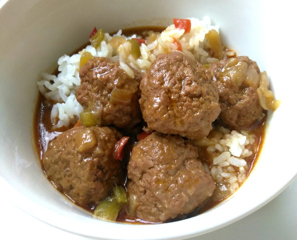A white bowl filled with rice and meatballs cooked in a dark roux.
