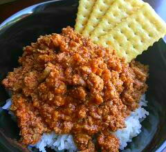 Black bowl on a counter top filled with Chili over rice and crackers.