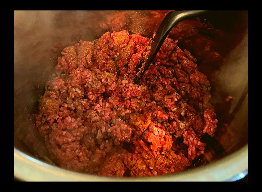 The inside of an Instant Pot filled with raw ground meat being browned.