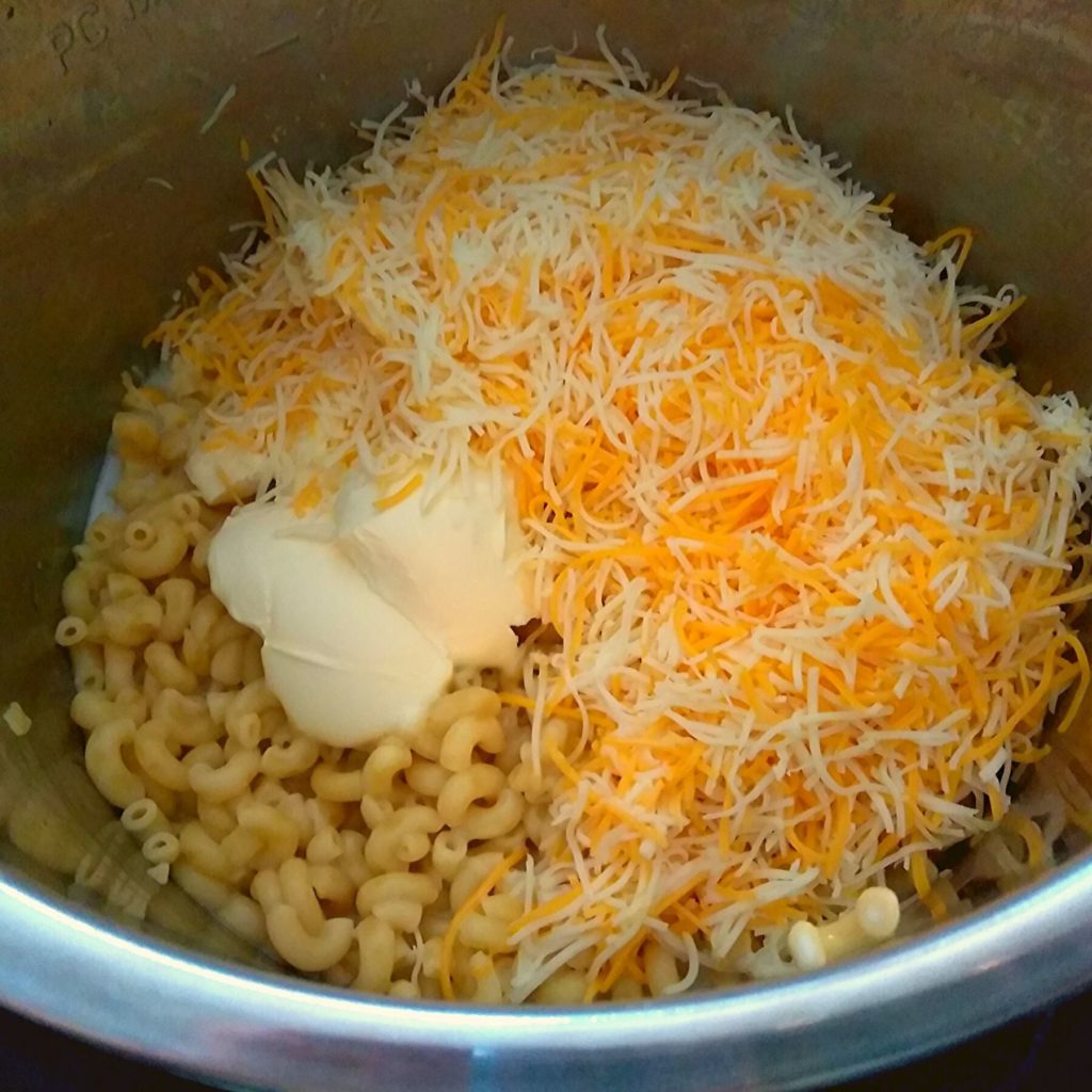 A Instant Pot filled with cooked elbow noodles, butter, shredded cheese, and milk not mixed together.