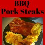 A black plate with bbq pork steak, garlic bread, and potato salad.