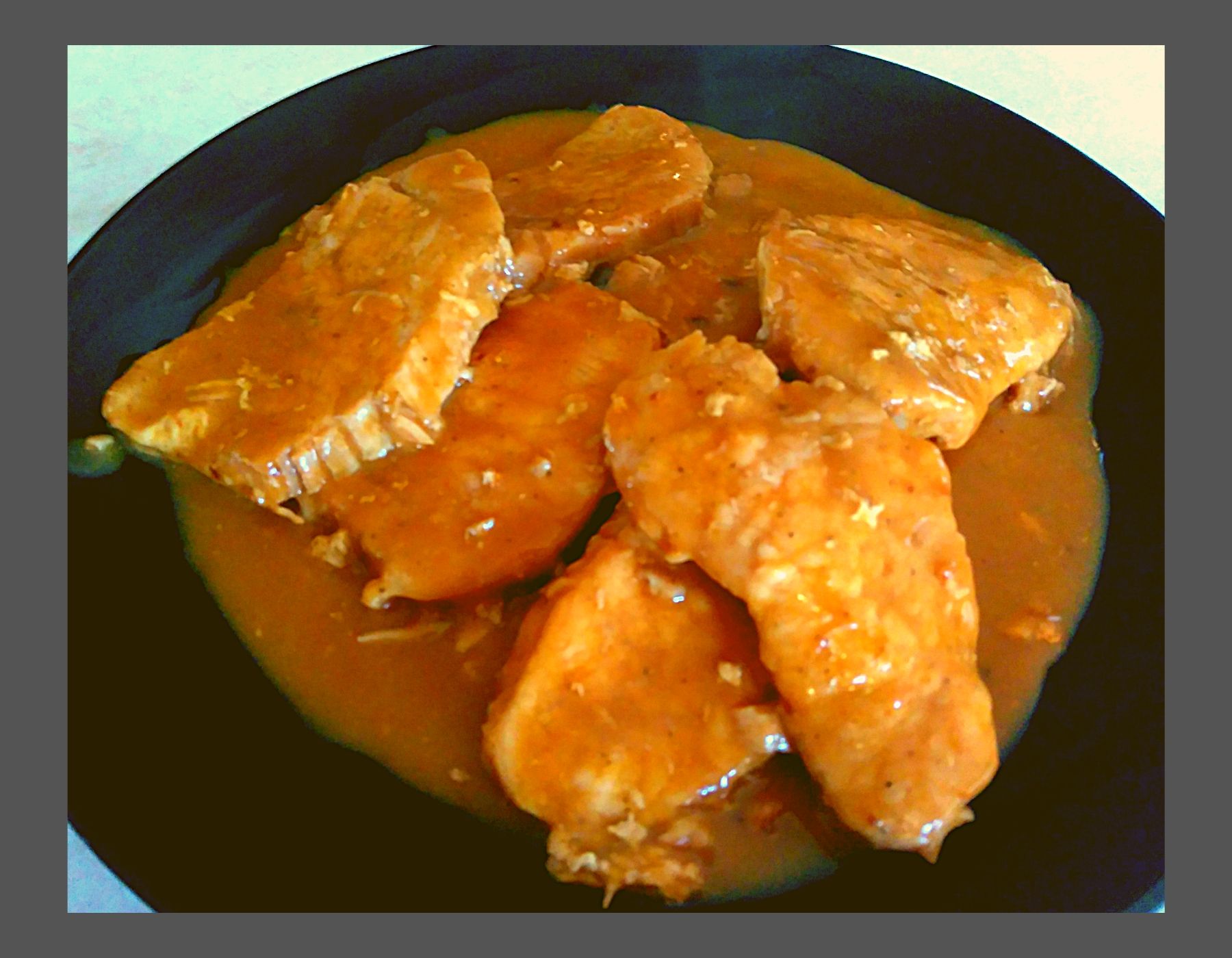 A black plate with pork chops covered in gravy.