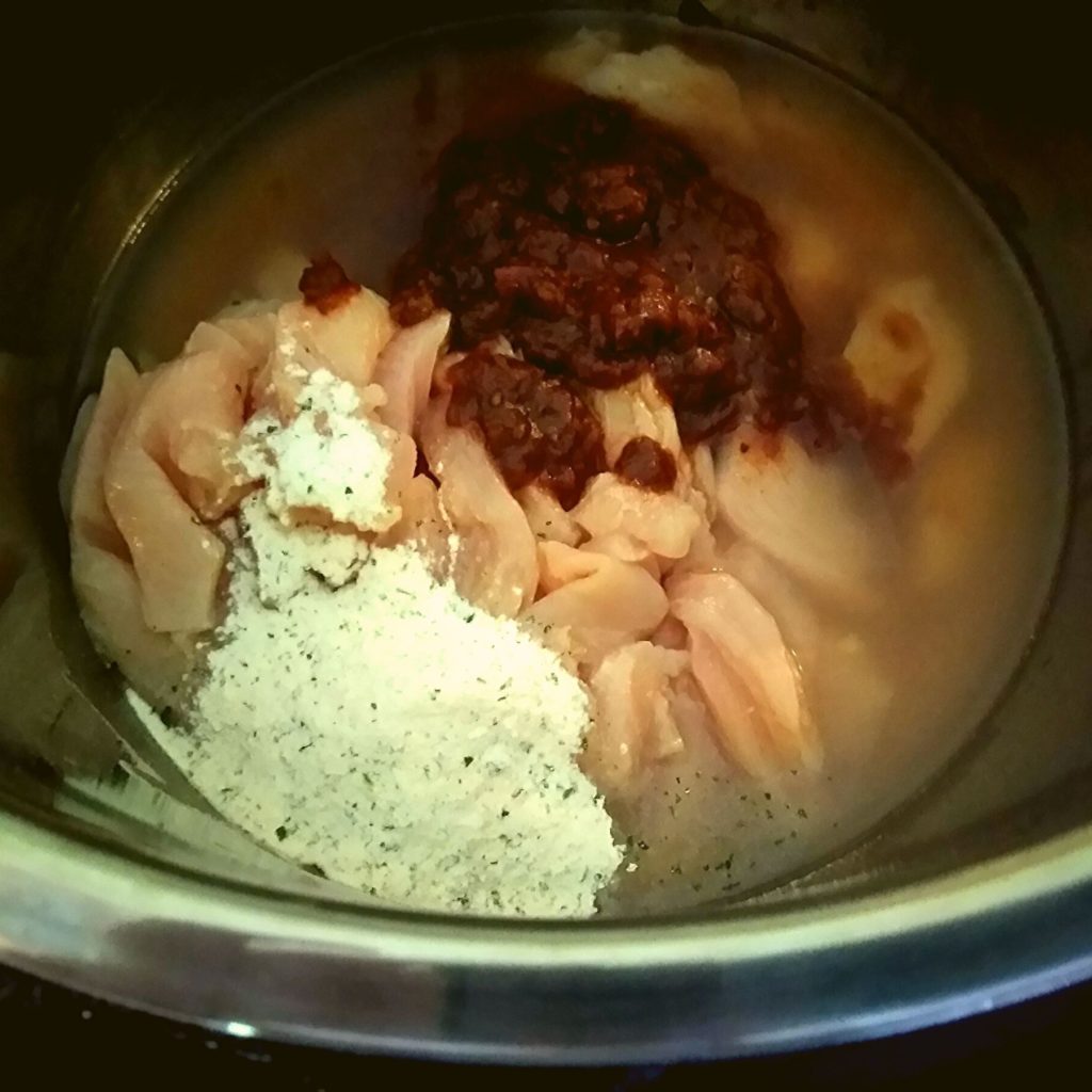 An Instant Pot filled with water, raw chicken breast, dry ranch dressing mix, and frontera taco sauce.