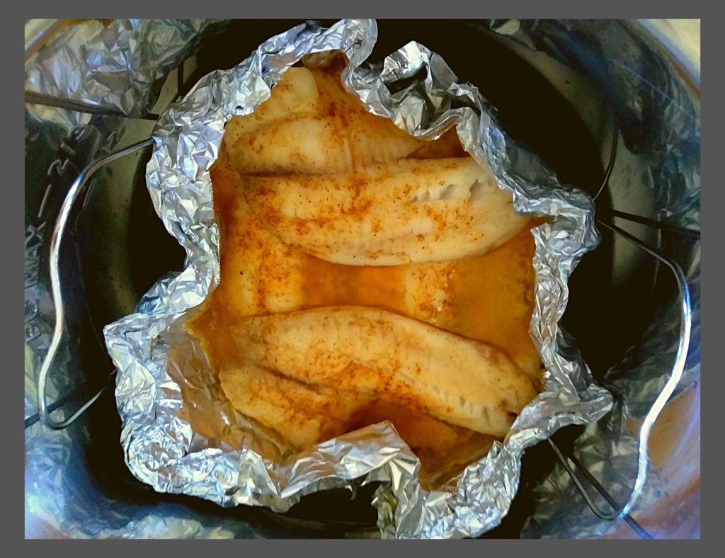 Cooked tilapia fillets inside a foil boat resting in an instant pot.