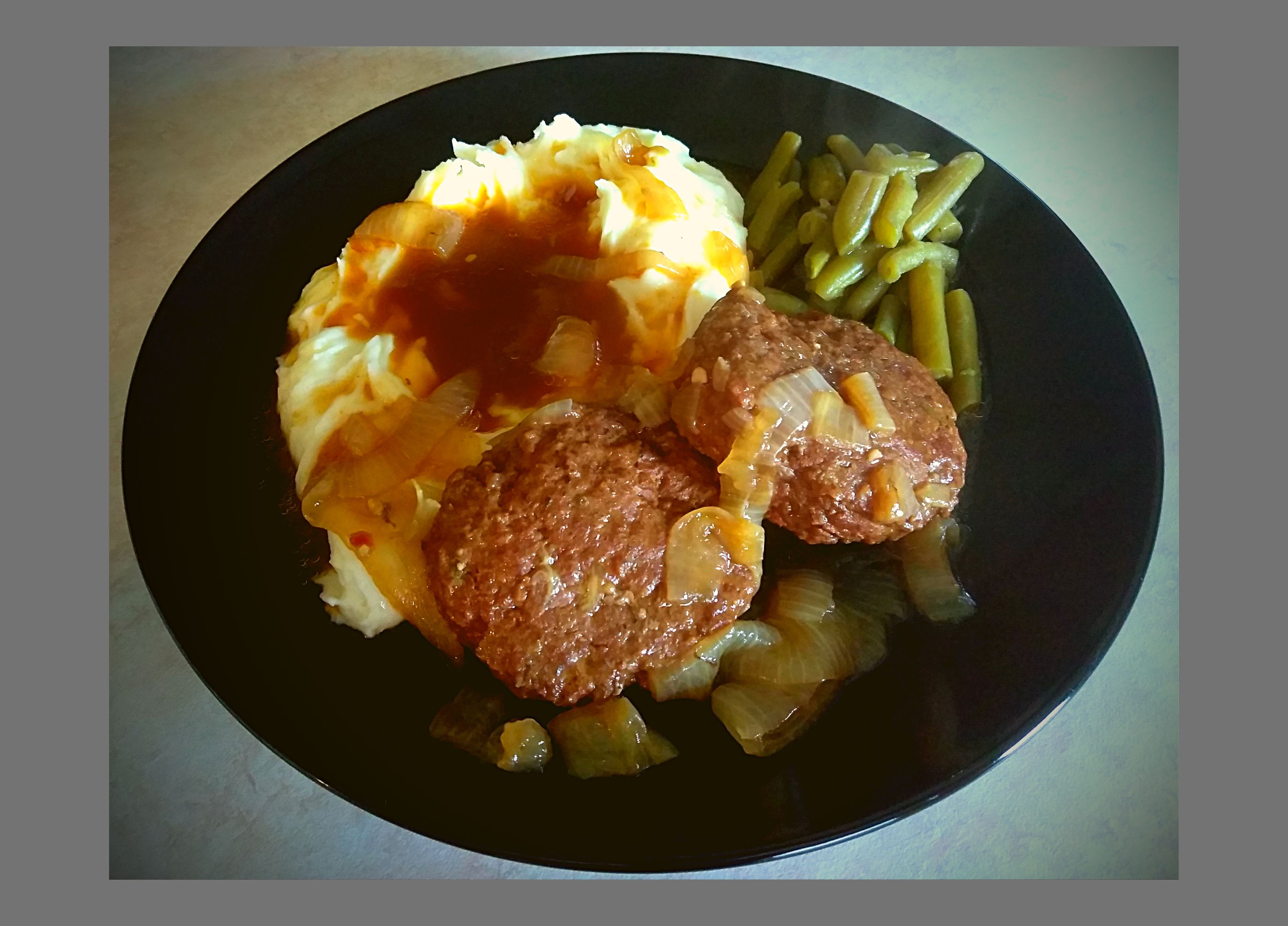 A black plate filled with instant Pot salisbury steak and greavy over mashed potatoes with green beans.