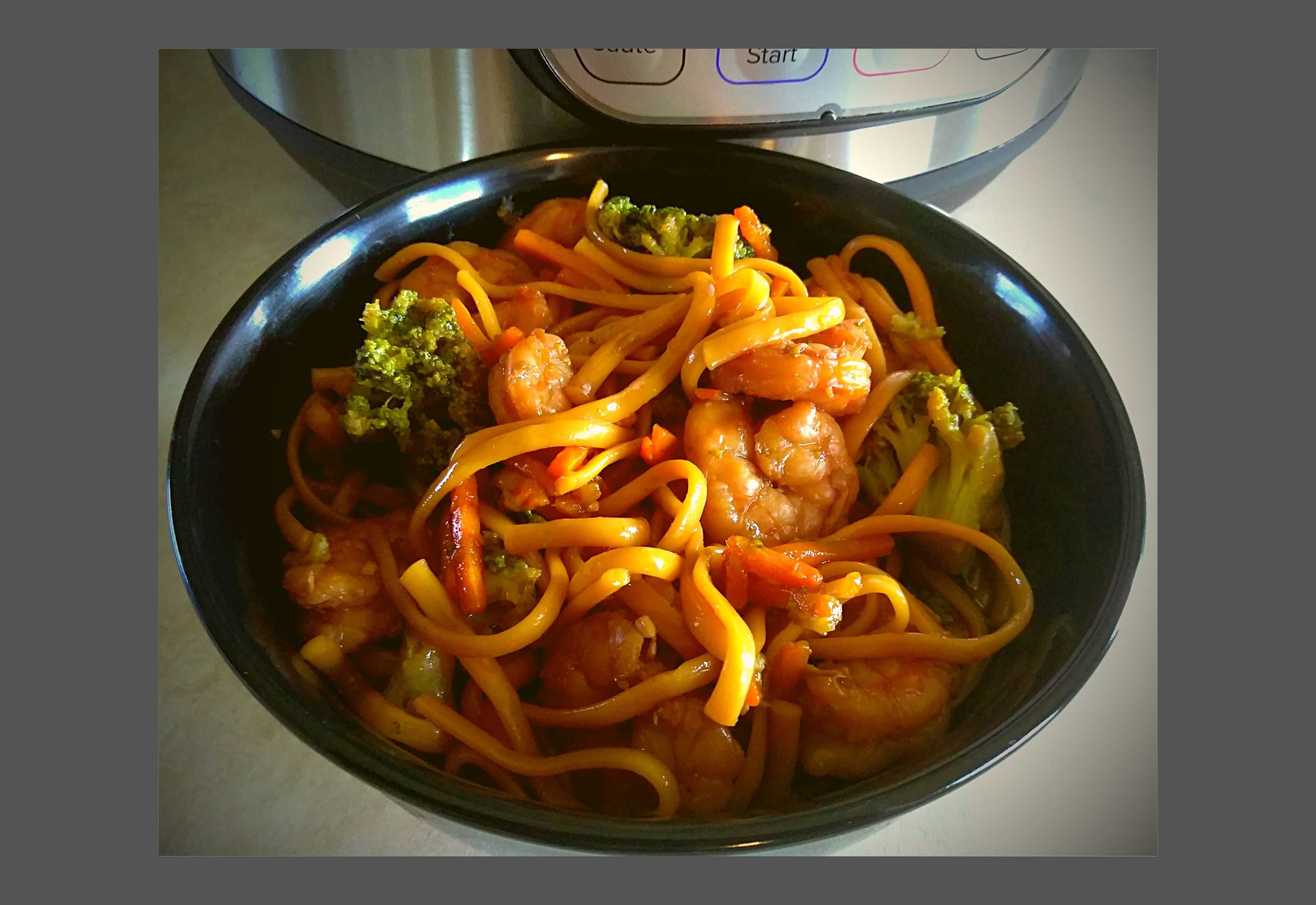 A black bowl filled with Instant Pot Shrimp lo mein with broccoli and carrots.