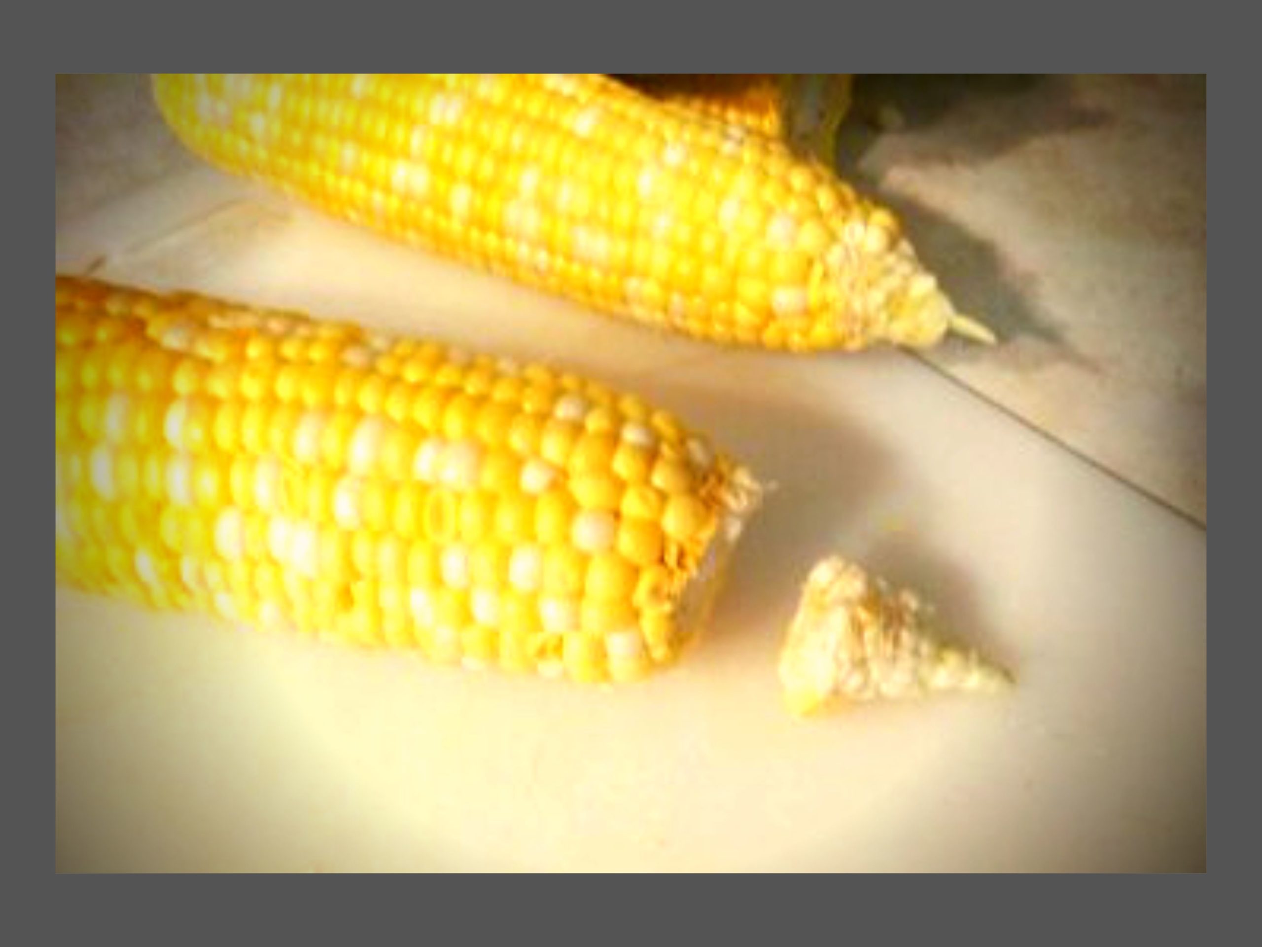 Two whole ears of corn on a cutting board. One with the tip cut off.