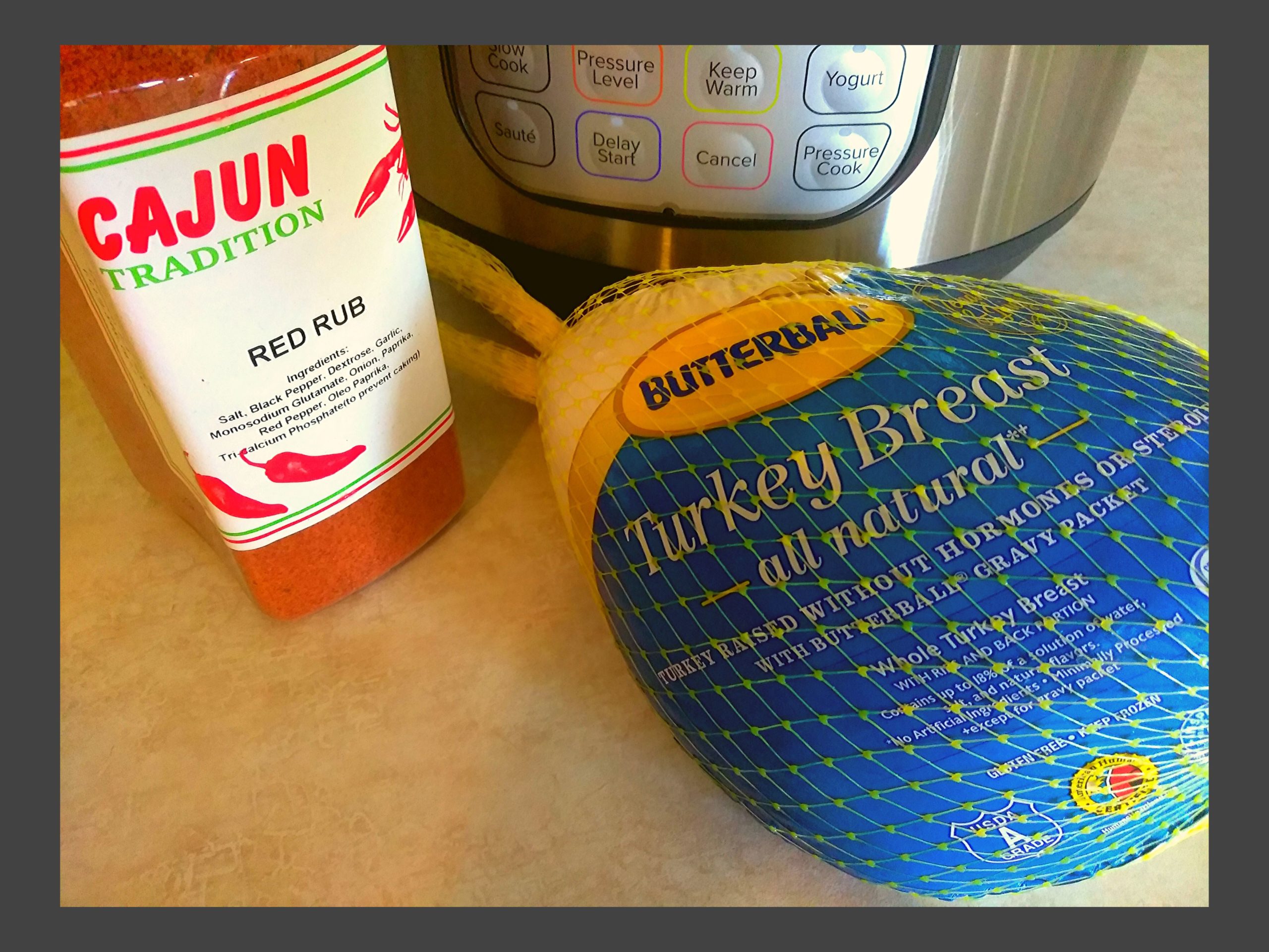 A container of red rub seasoning, a frozen butterball turkey breast in the wrapper, sitting in front of an Instant Pot.
