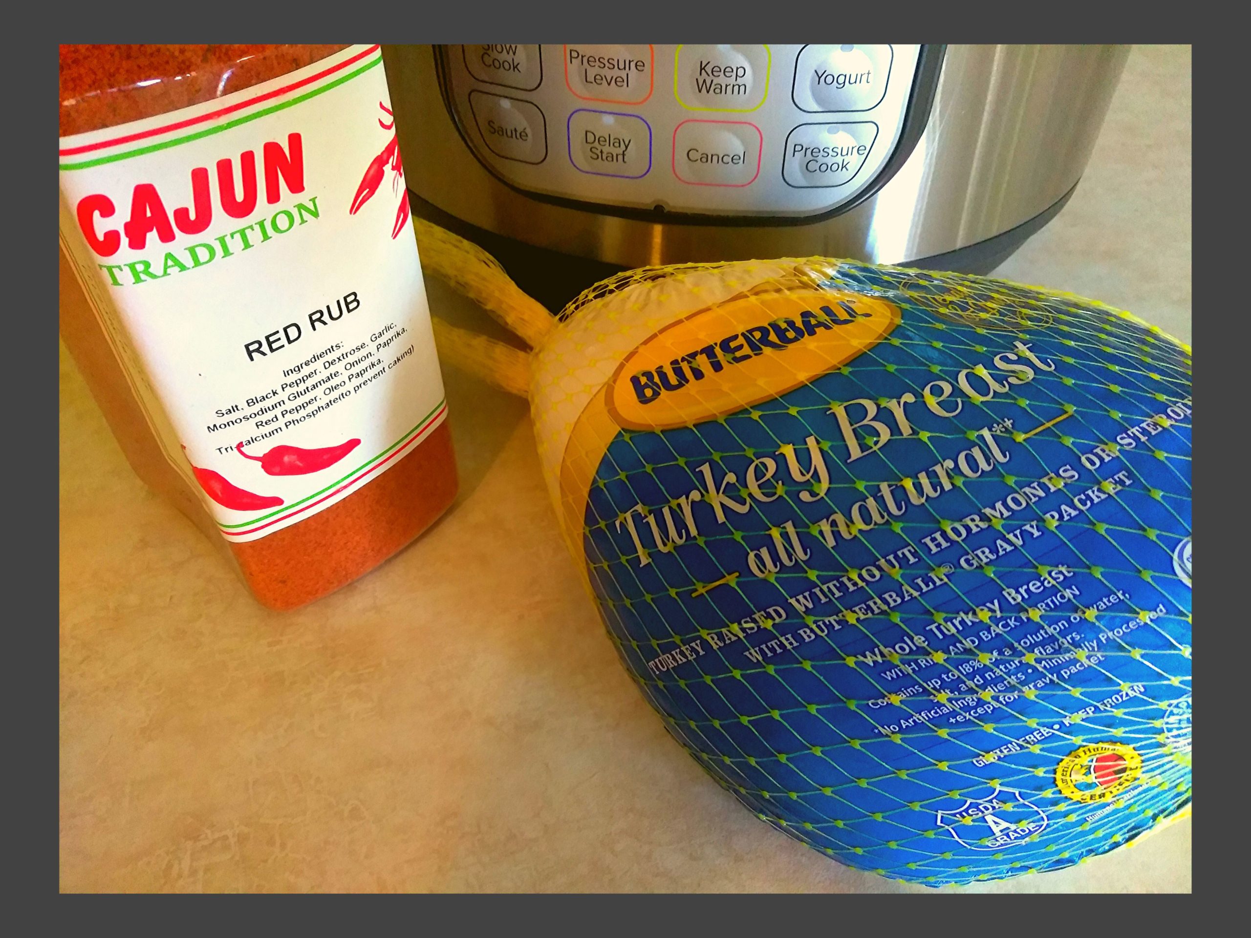 A container of red rub seasoning, a frozen butterball turkey breast in the wrapper, sitting in front of an Instant Pot.