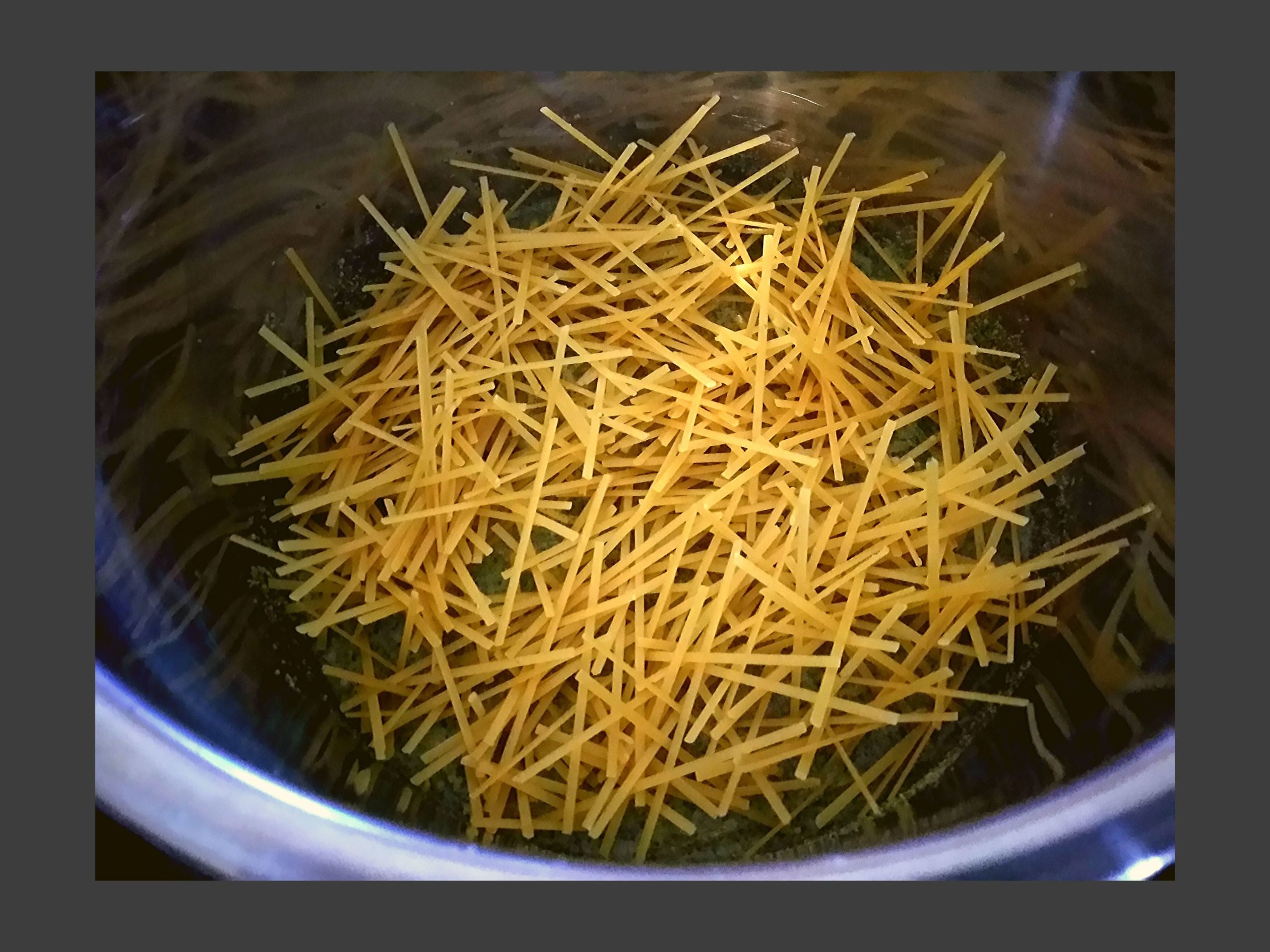 Inside of a silver instant pot with broken, uncooked linguine noodles in a messy fashion.