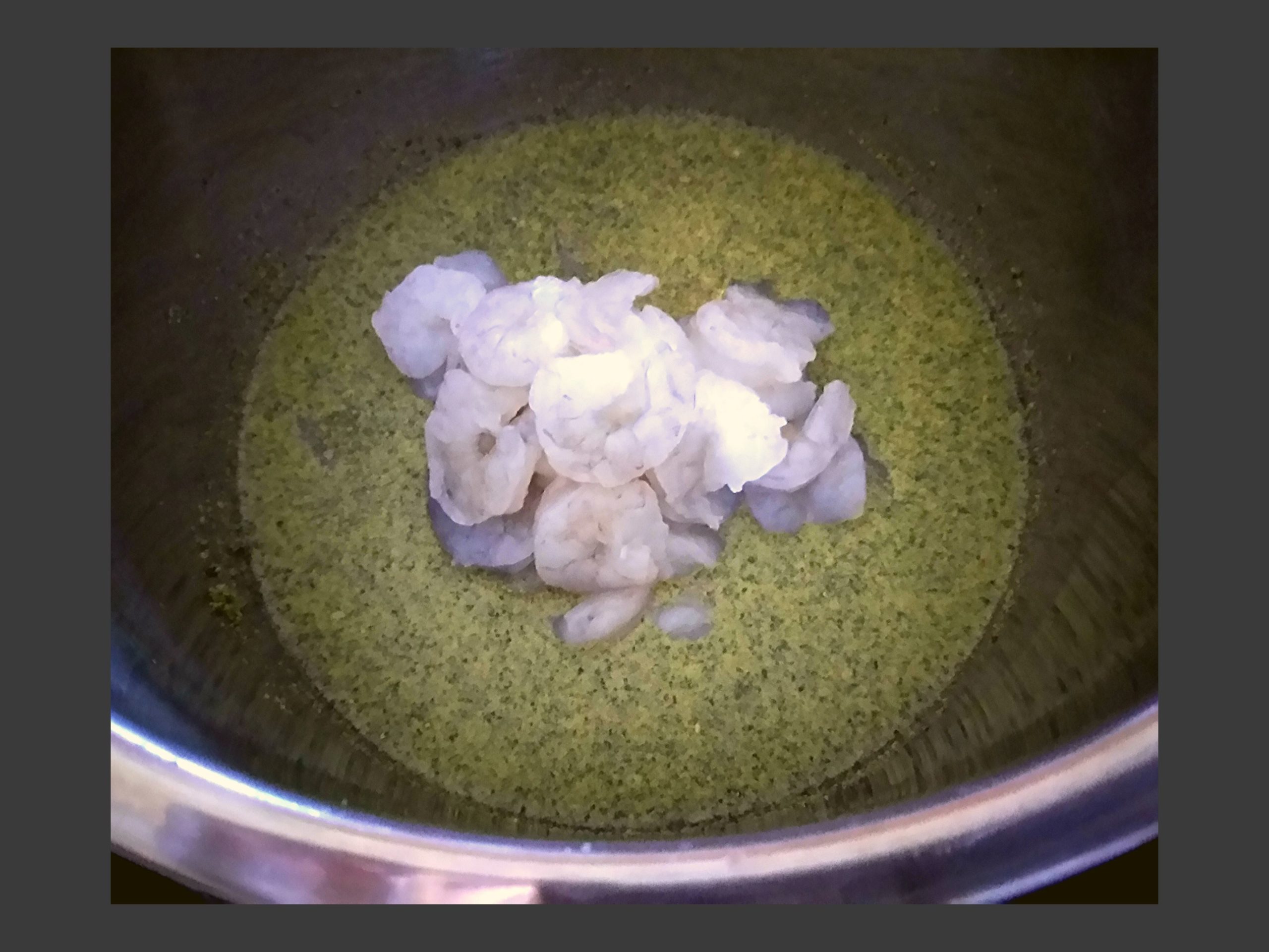 The inside of an Instant Pot filled with raw shrimp, chicken broth, and garlic butter shrimp scampi seasoning.