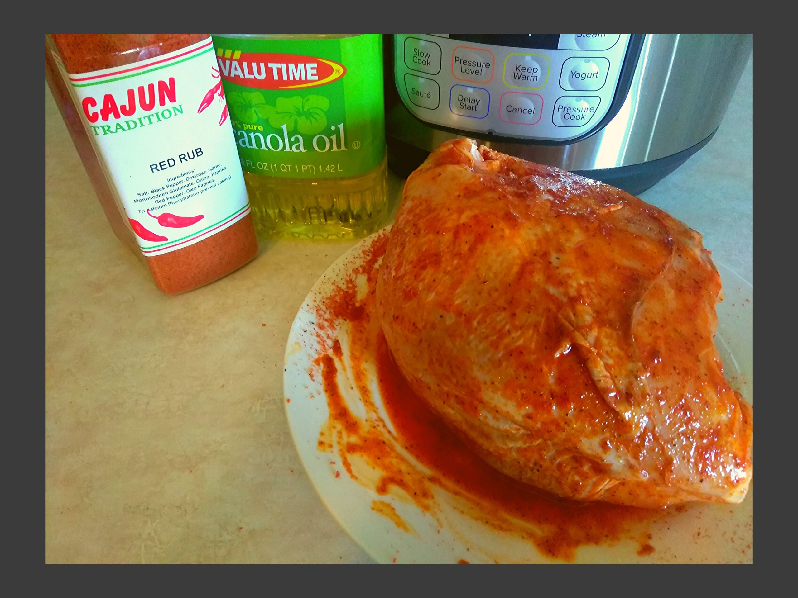 A raw turkey breast covered in oil and red rub seasoning sitting on a white plate in front of an Instant Pot.