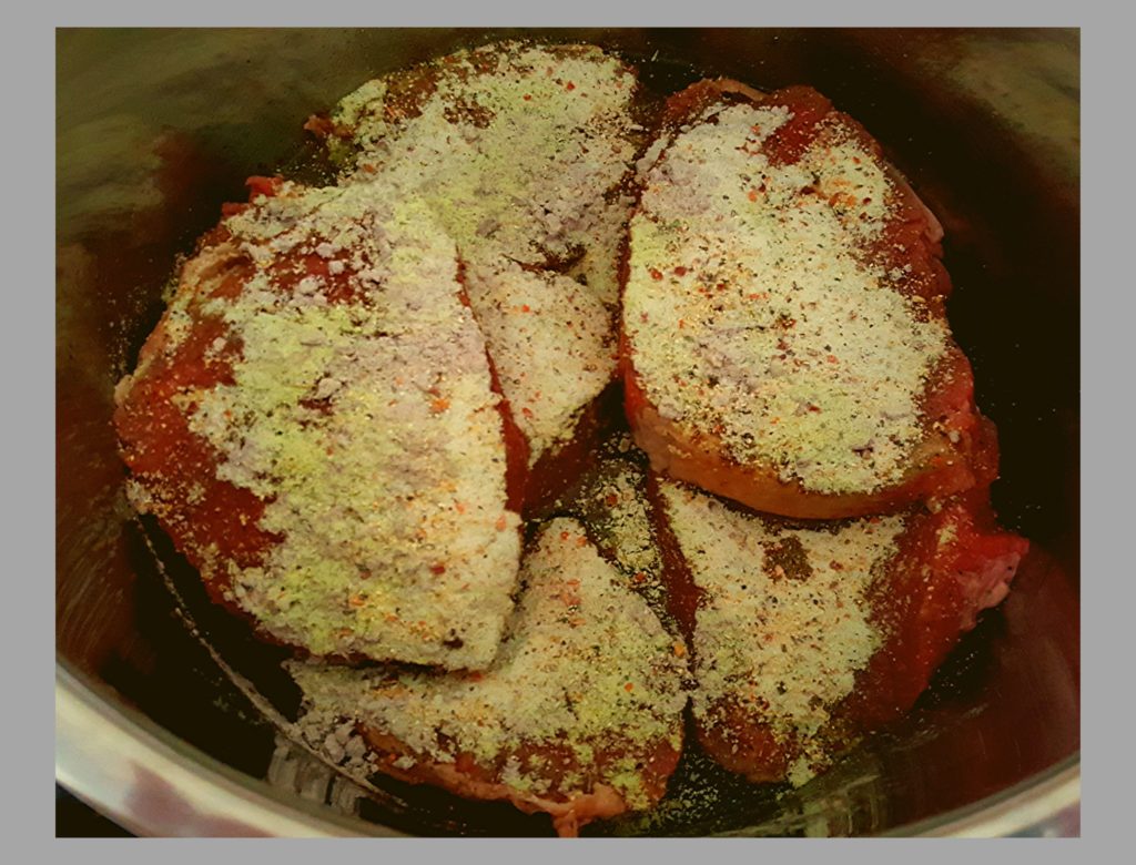 The inside of an Instant Pot with raw beef roast topped with 3 packets of powder ranch, italian, and brown gravy.