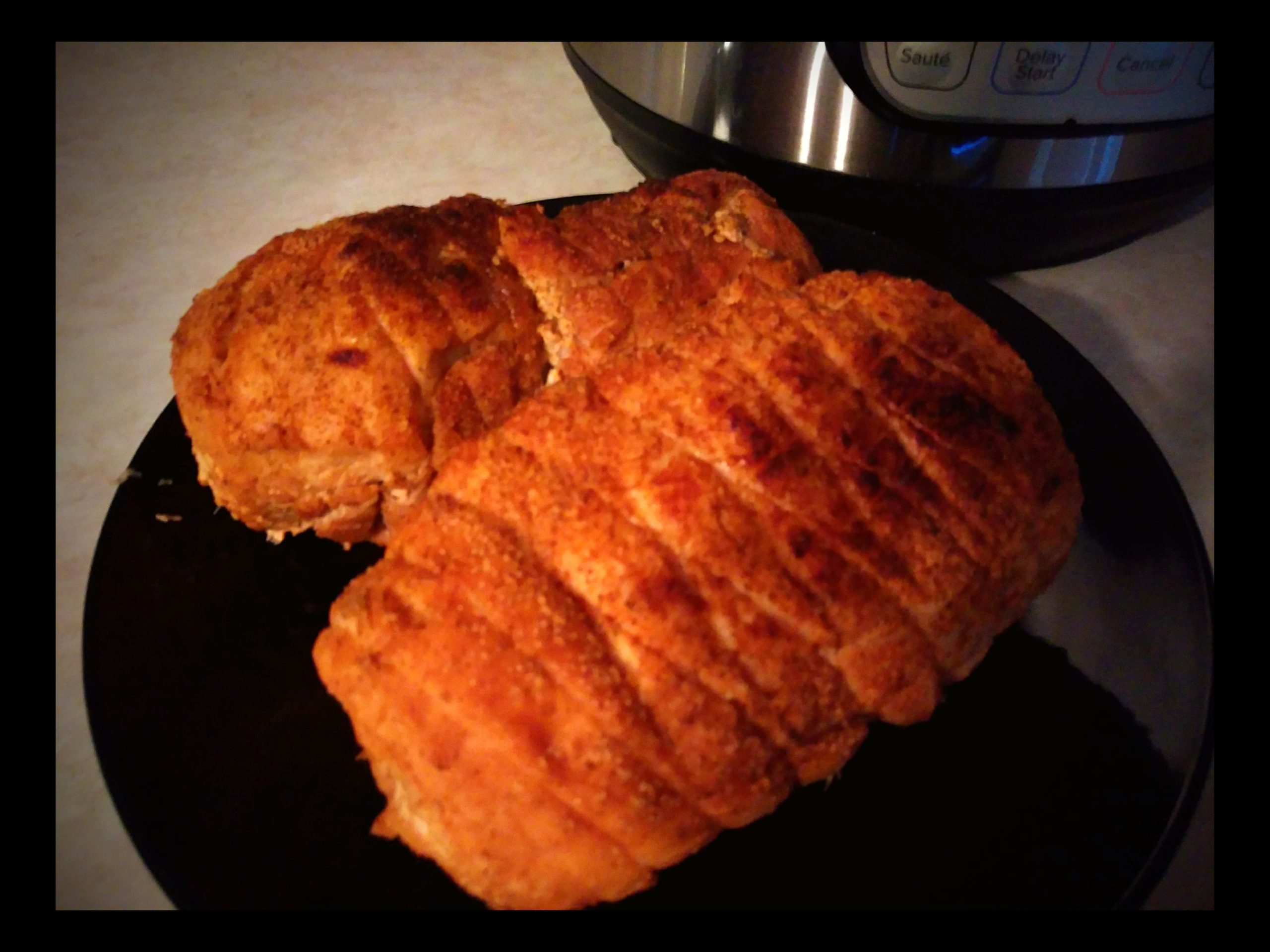 A black plate with two cooked turkey roasts on a counter in front of an Instant Pot.