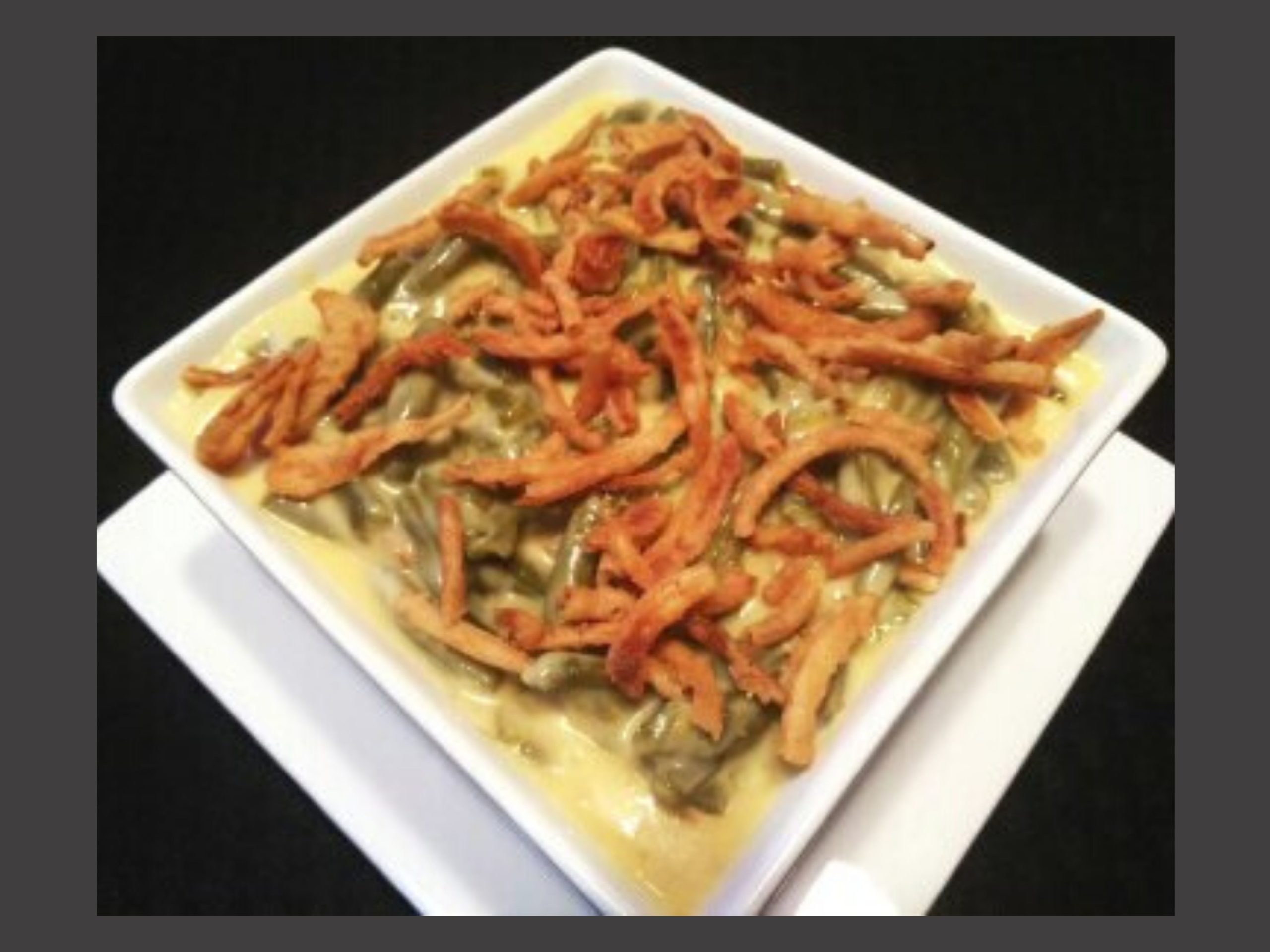 A square white bowl filled with green bean casserole.