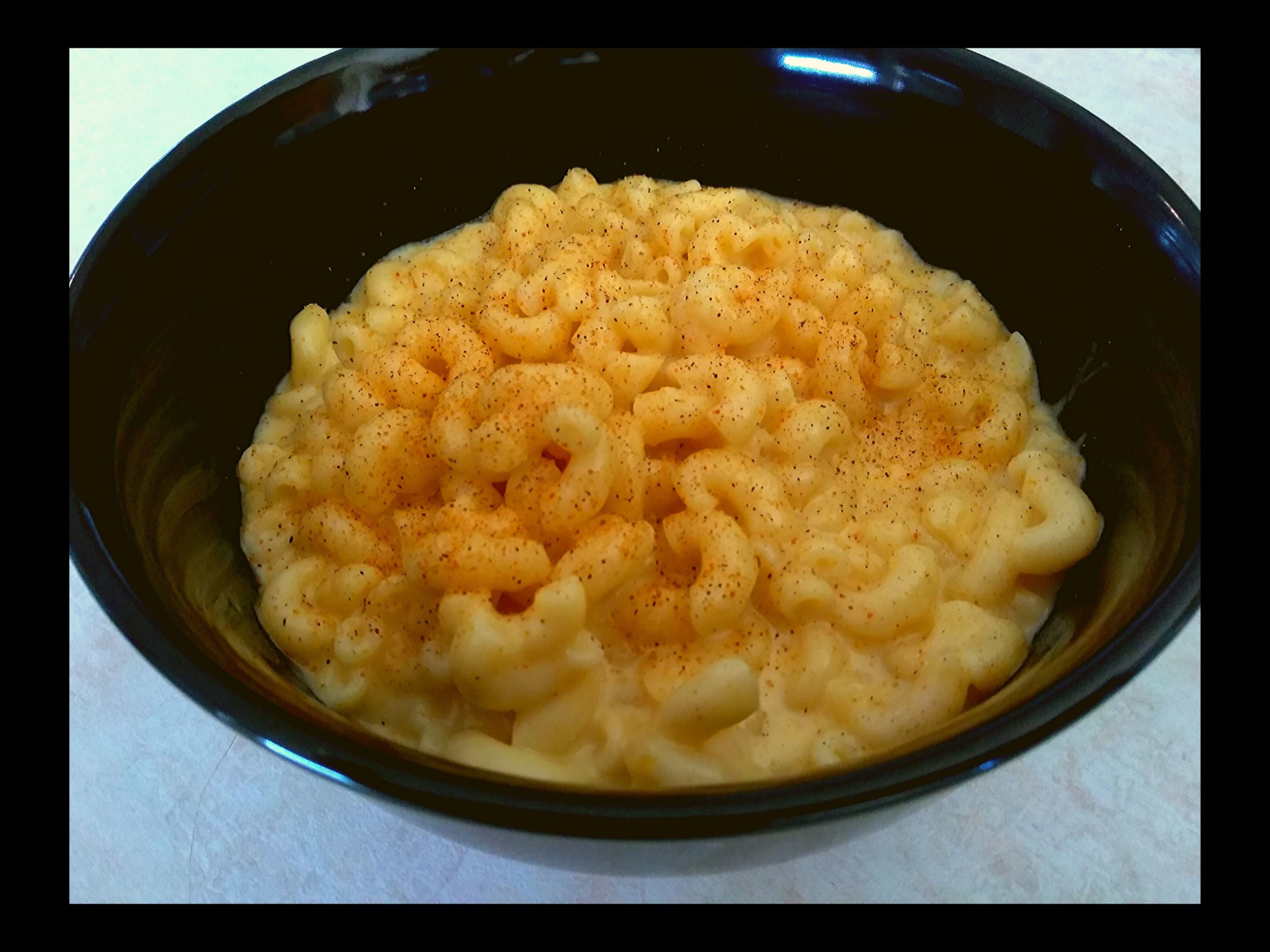 A black bowl filled with macaroni and cheese.