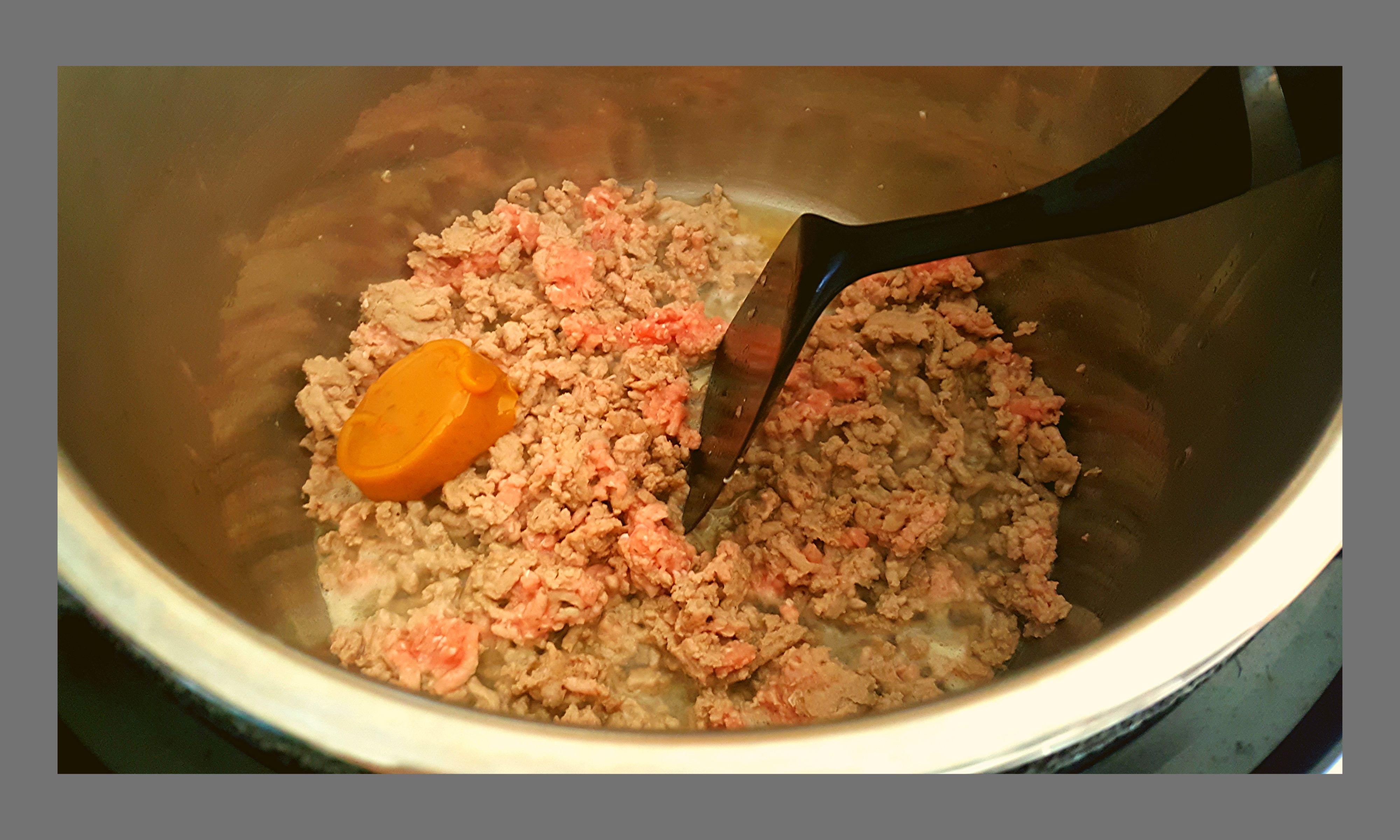 The inside of a silver Instant pot filled with raw ground turkey and a Knorr Chicken stock concetrate while it is browning.