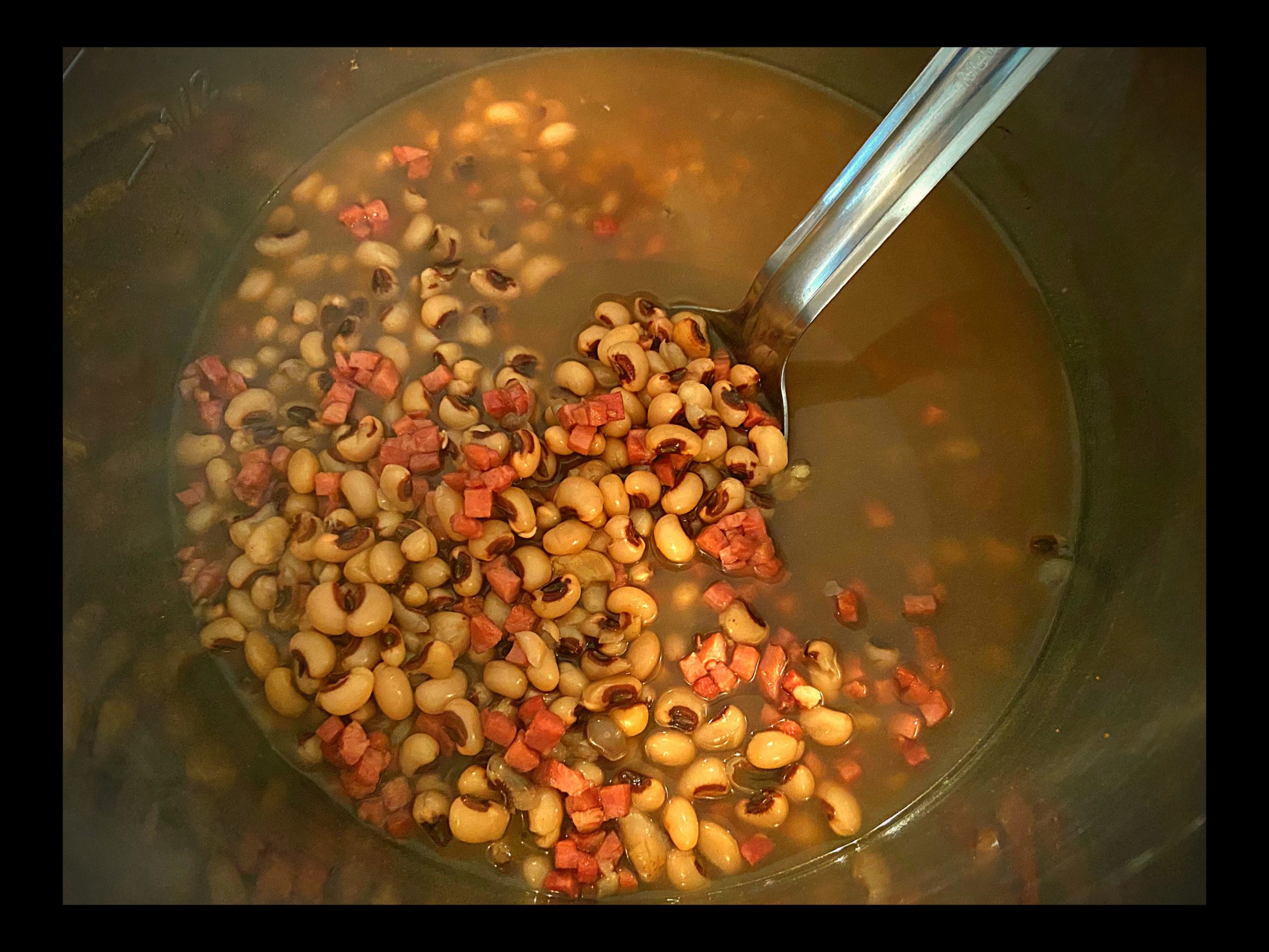 The inside of an Instant Pot filled with cooked southern black eyed peas and ham with a large silver spoon.