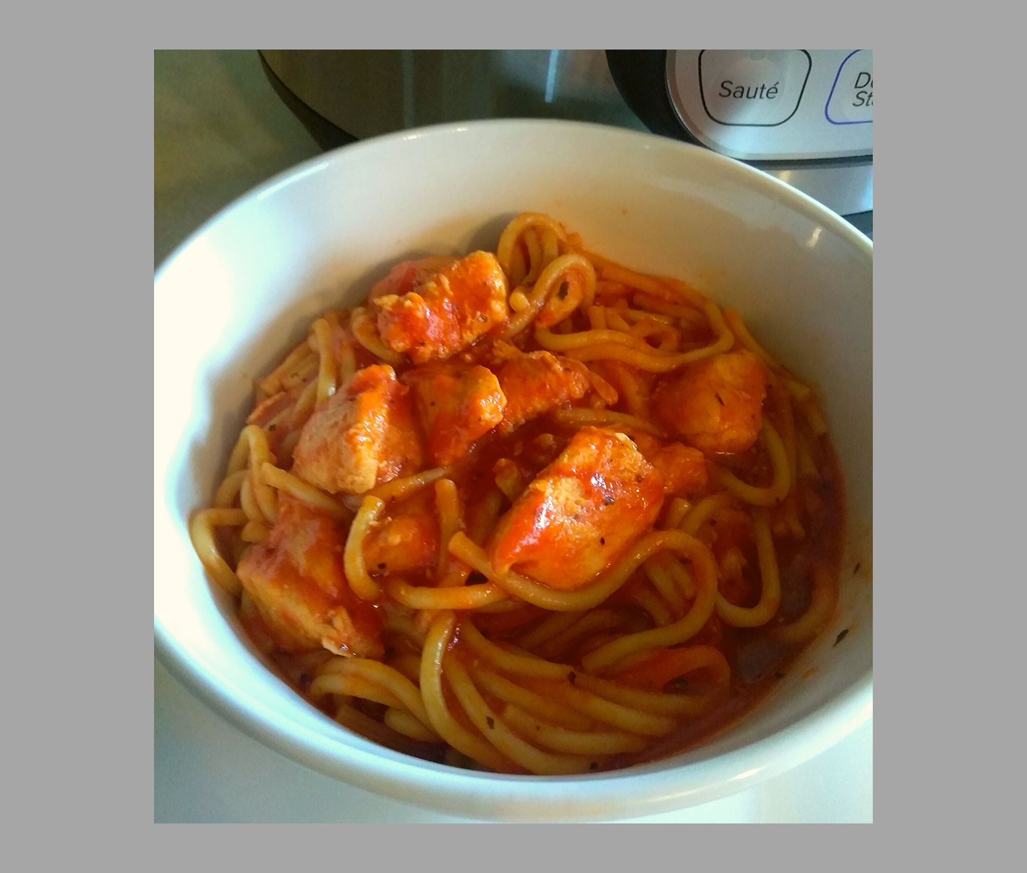 A white bowl filled with chicken spaghetti sitting on a kitchen counter.