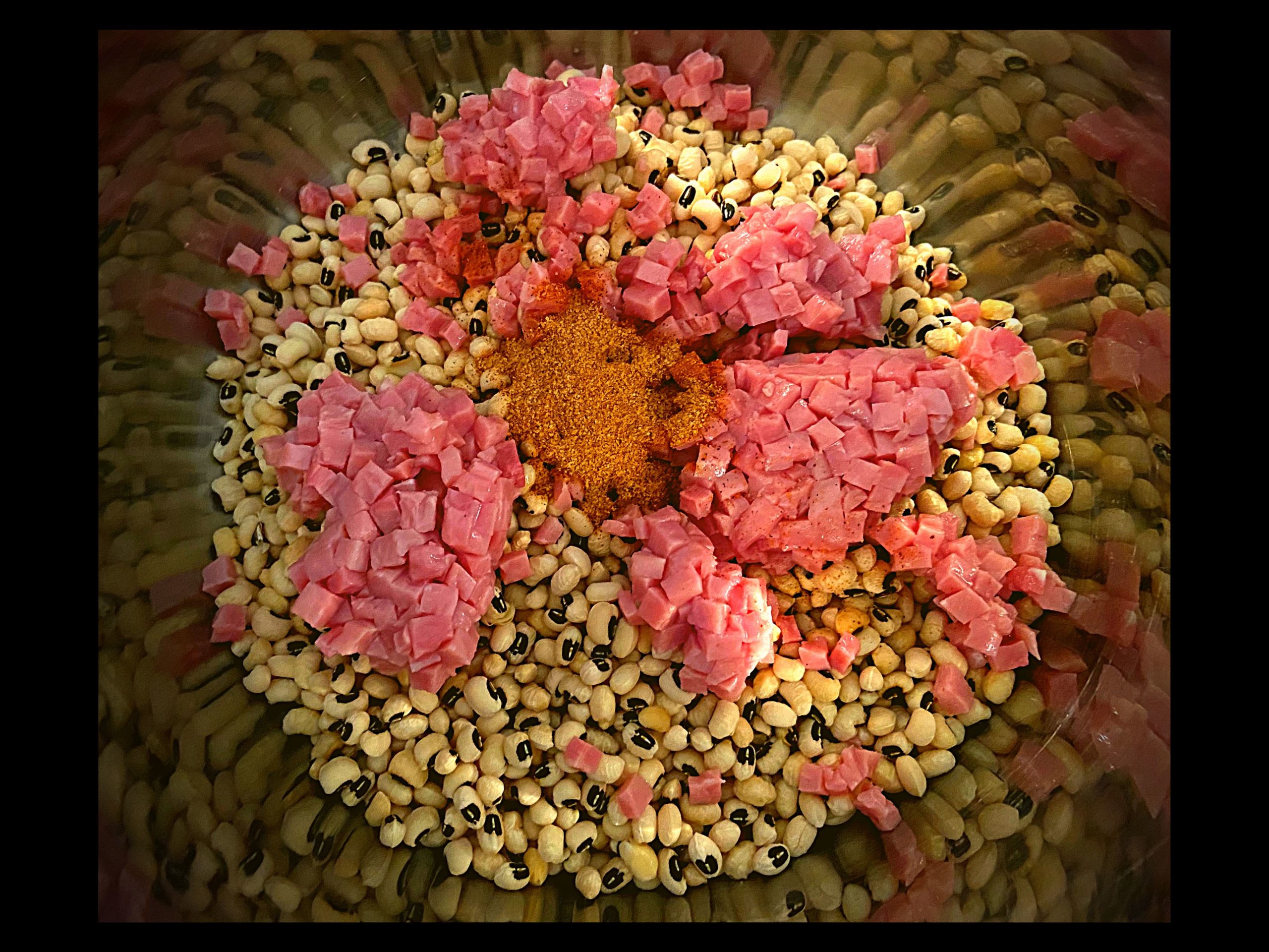 The inside of an Instant Pot filled with dry black eyed peas, diced ham, and 1 tbsp. of Tony Chachere's Seasoning not stirred together.