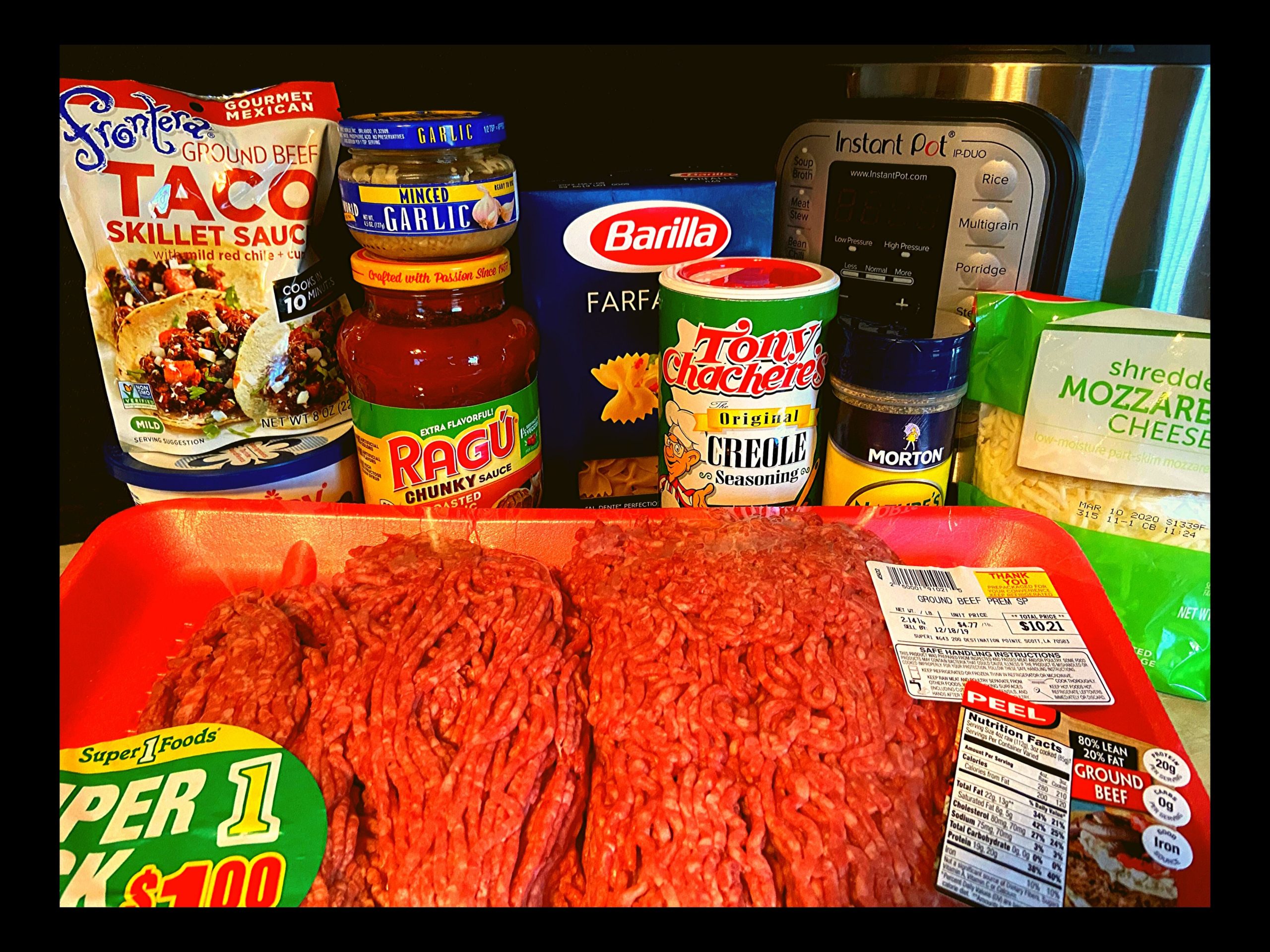 A packet of raw ground meat, frontera taco sauce packet, container of cottage cheese, container of minced garlic, ragu spaghetti sauce, box of bow tie pasta, tony chachere's seasoning, nature seasoning, and shredded mozzerela cheese all sitting on a kitchen counter top in front of an Instant Pot.