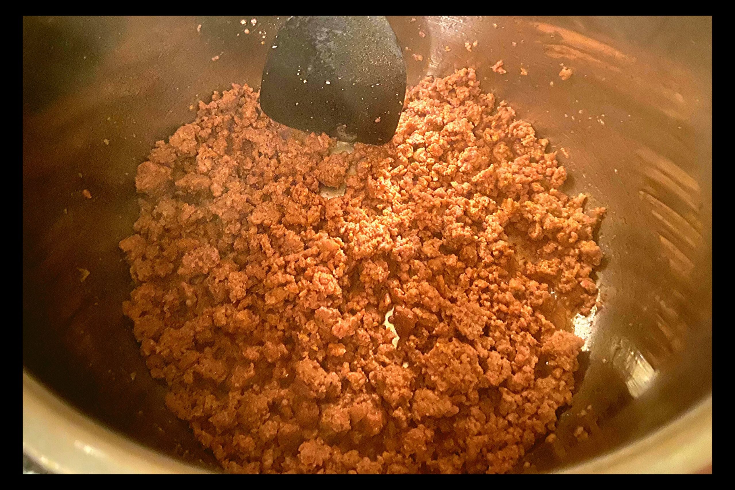 The inside of a silver Instant Pot filled with browned ground meat.
