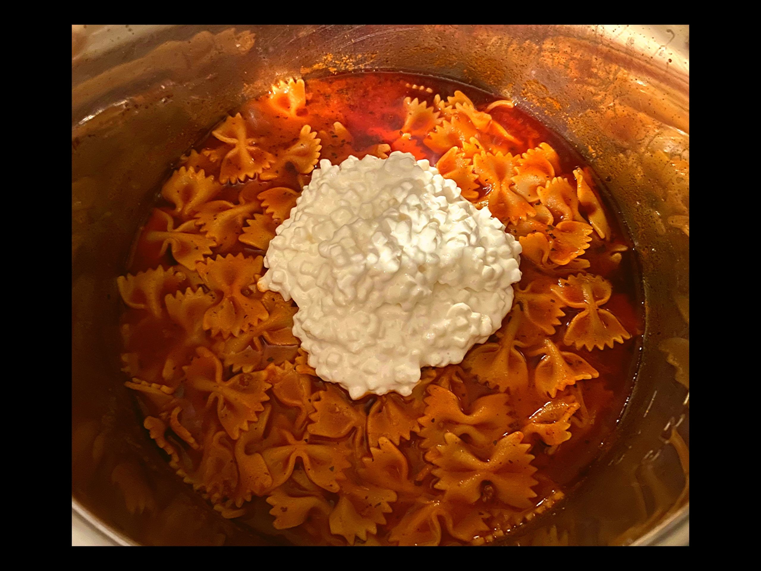 Instant Pot filled with bow tie pasta in spaghetti sauce with 1 cup of cottage cheese on top.