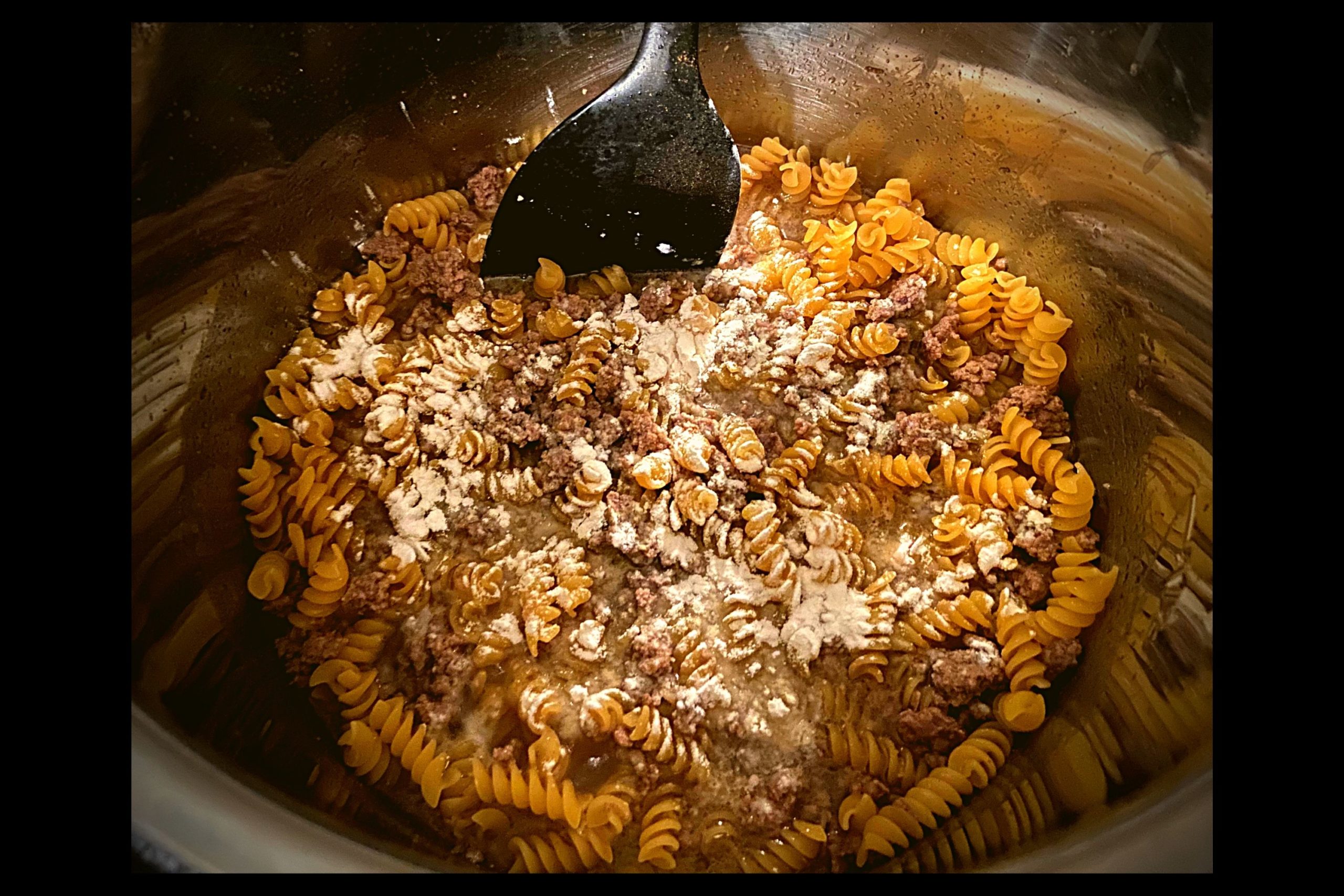 Instant Pot filled with ground meat, beef broth, rotini noodles, and topped with 1 tablespoon of flour