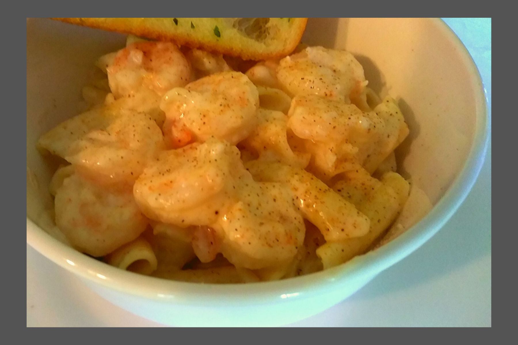 A white bowl filled with shrimp alfredo and penne pasta with garlic bread.