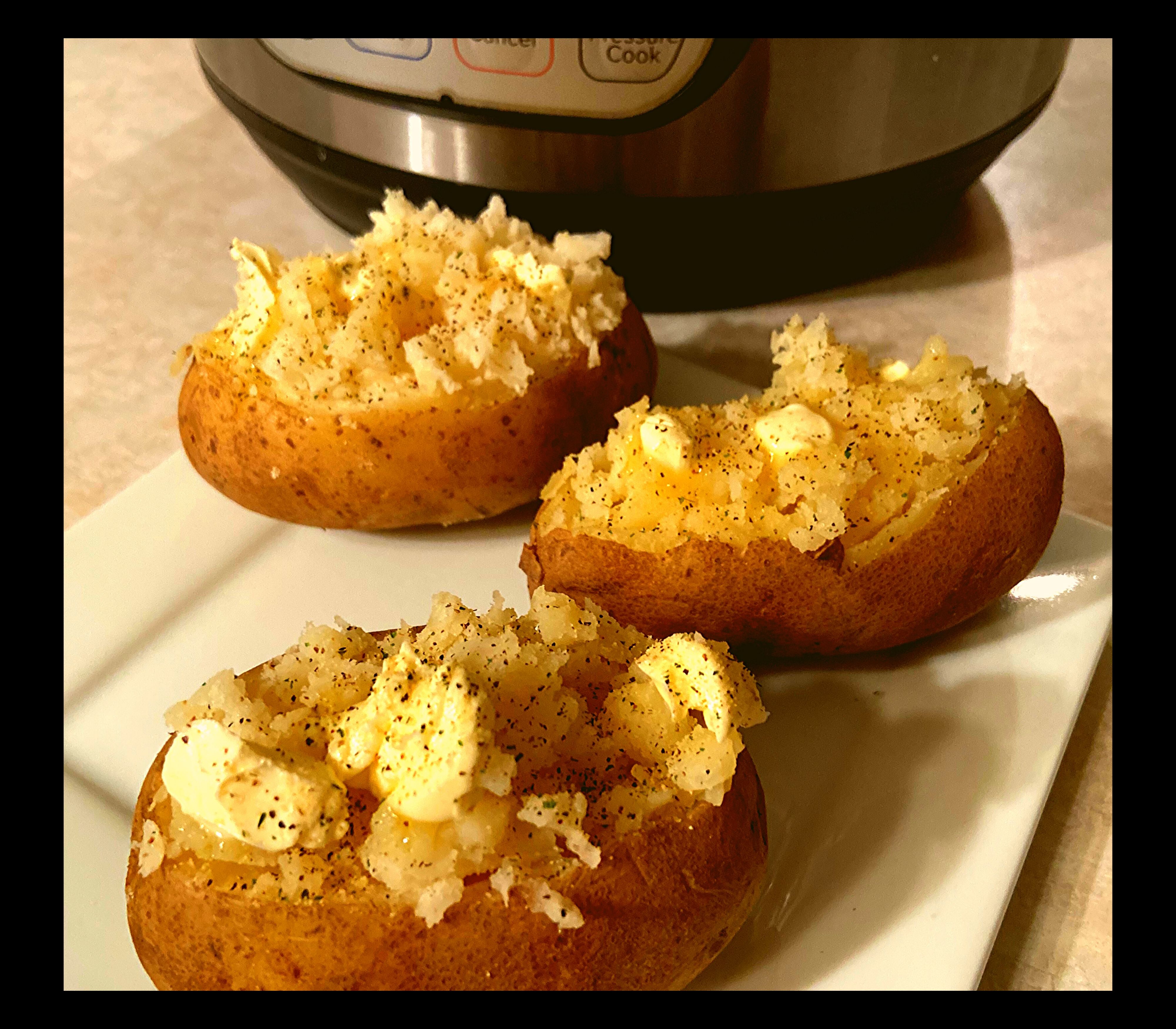 3 Instant Pot Baked Potatoes topped with butter, salt, and pepper on a square white plate sitting in front of an Instant Pot on a kitchen counter.