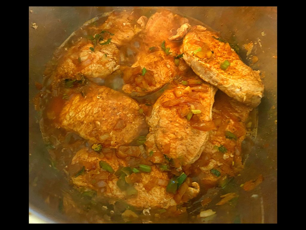 Beef broth and worcestershire sauce all mixed together with pork chops, onion, bell pepper, and onions in and Instant Pot