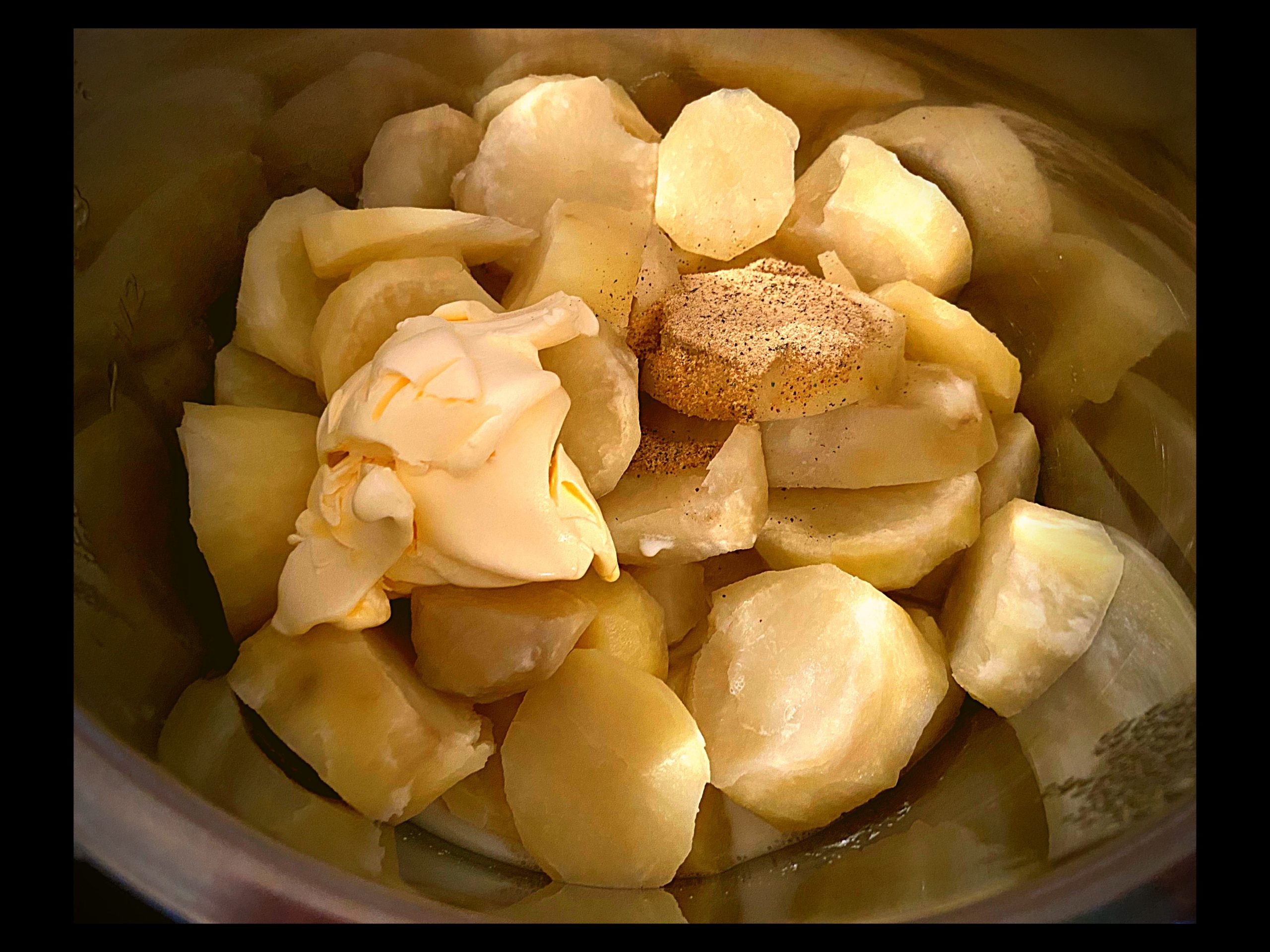 Cooked potatoes, spoonfulls of butter, milk, and nature seasoning inside of an Instant Pot pressure cooker