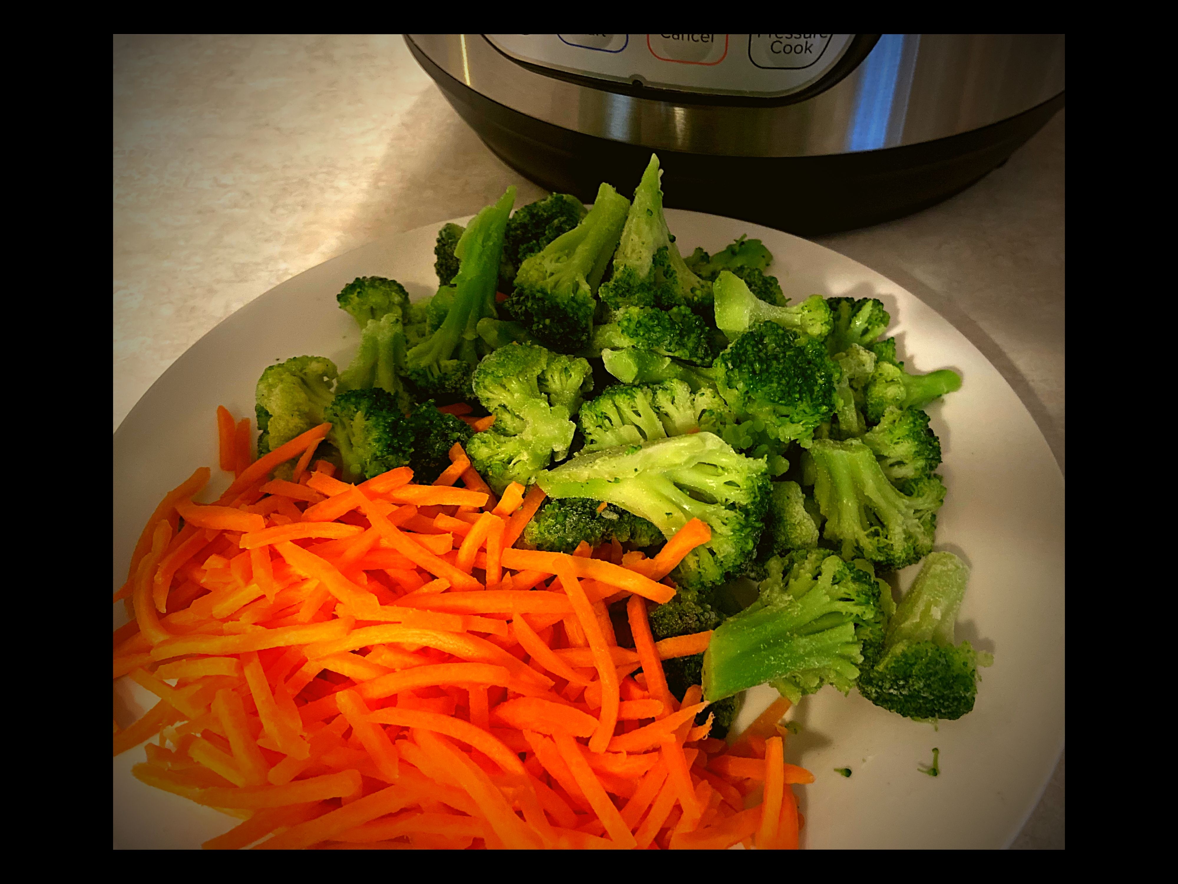 Matchstick carrotts and broccoli on a white plate in front of and Instant Pot