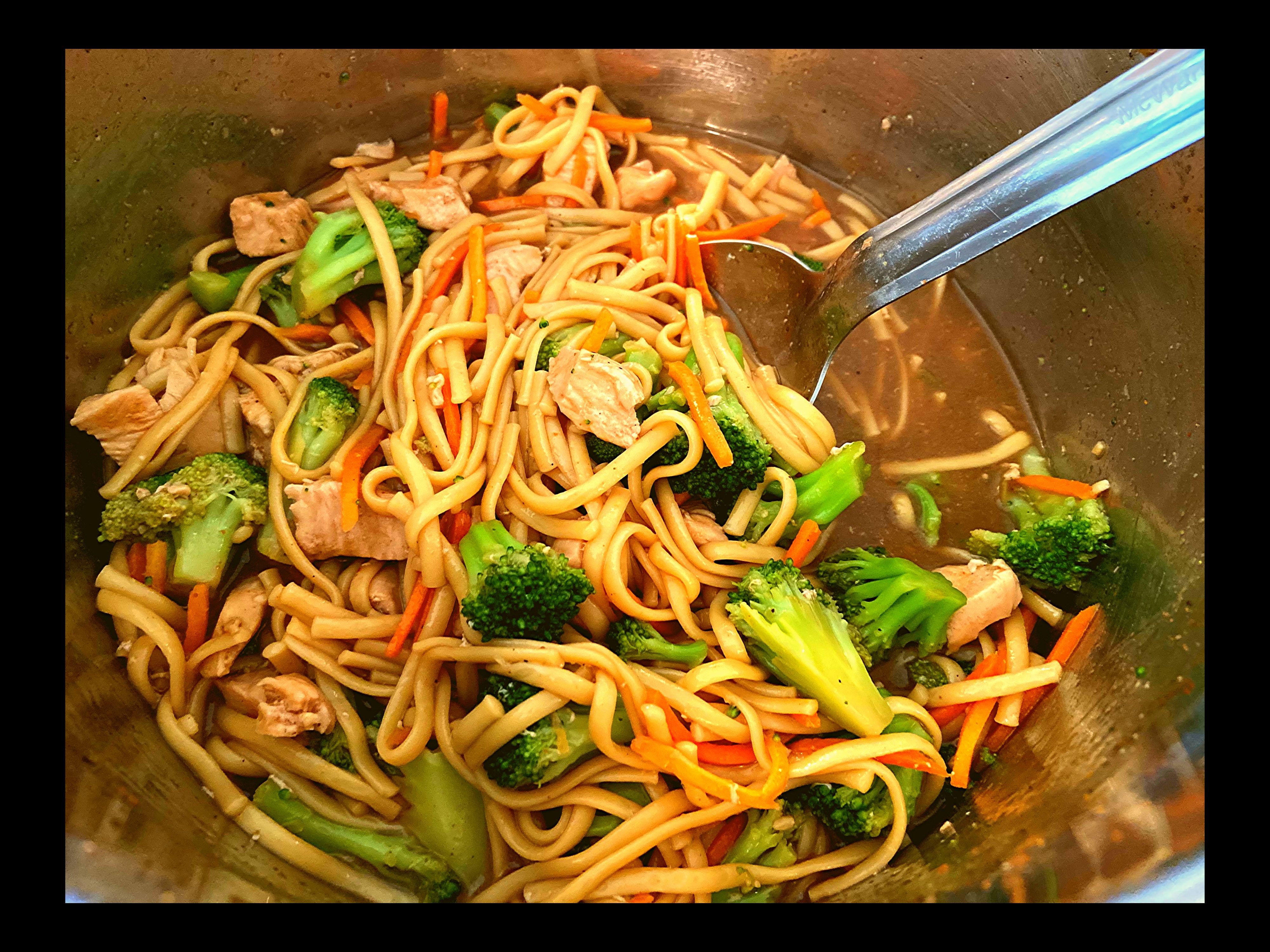 The inside of an Instant Pot filled with Instant Pot chicken lo mein and a big silver spoon.