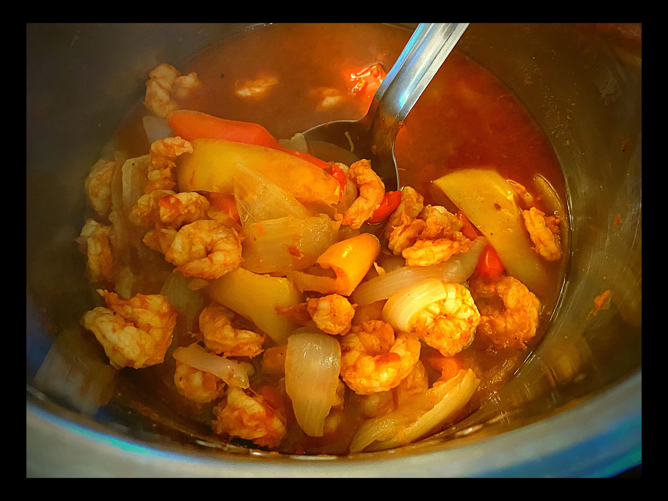 The inside of an Instant Pot filled with cooked shrimp, onions, and bell peppers in a red fajita sauce.