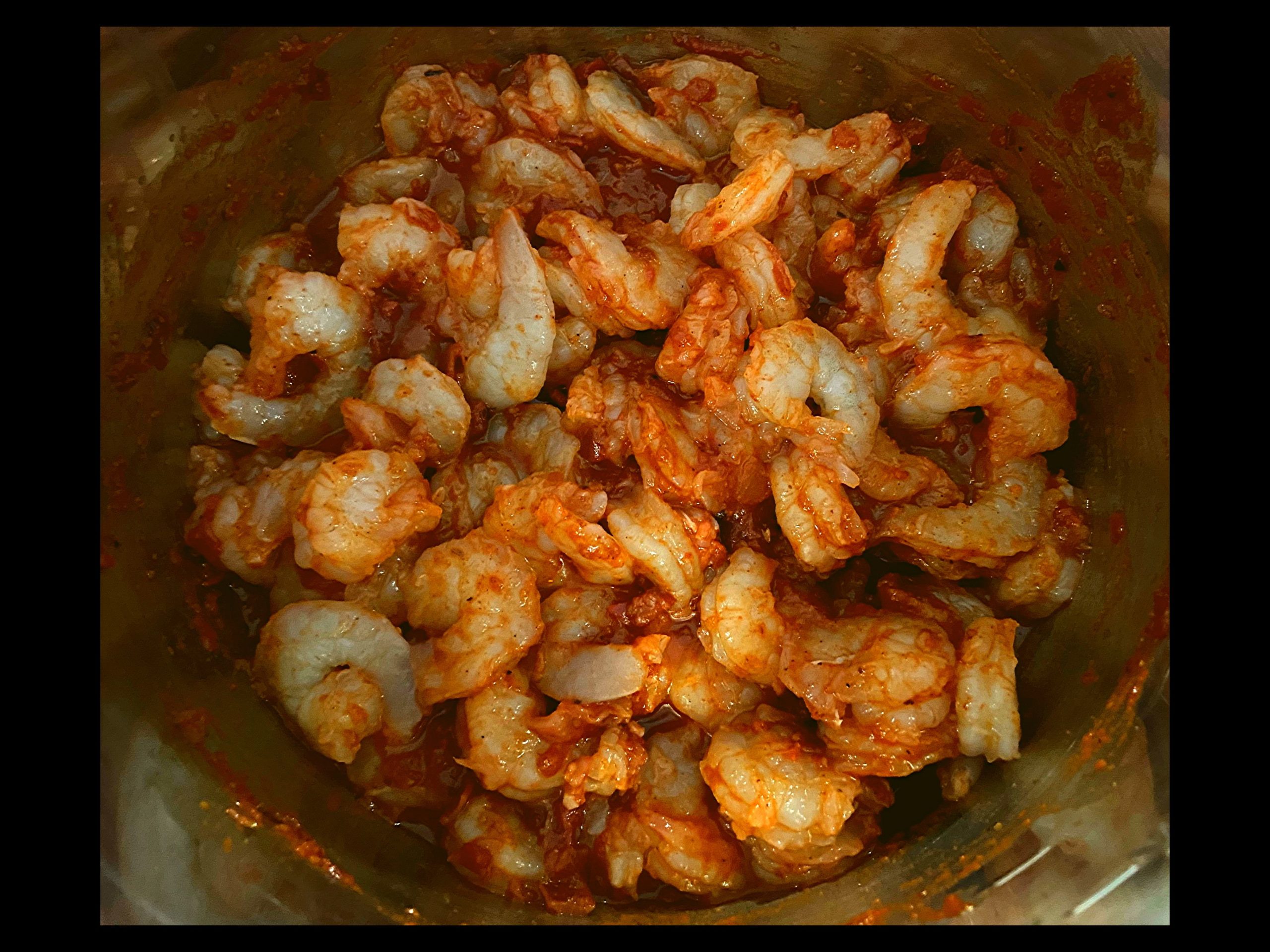 The inside of an Instant pot filled with large raw peeled shrimp mixed together with Frontera taco sauce.