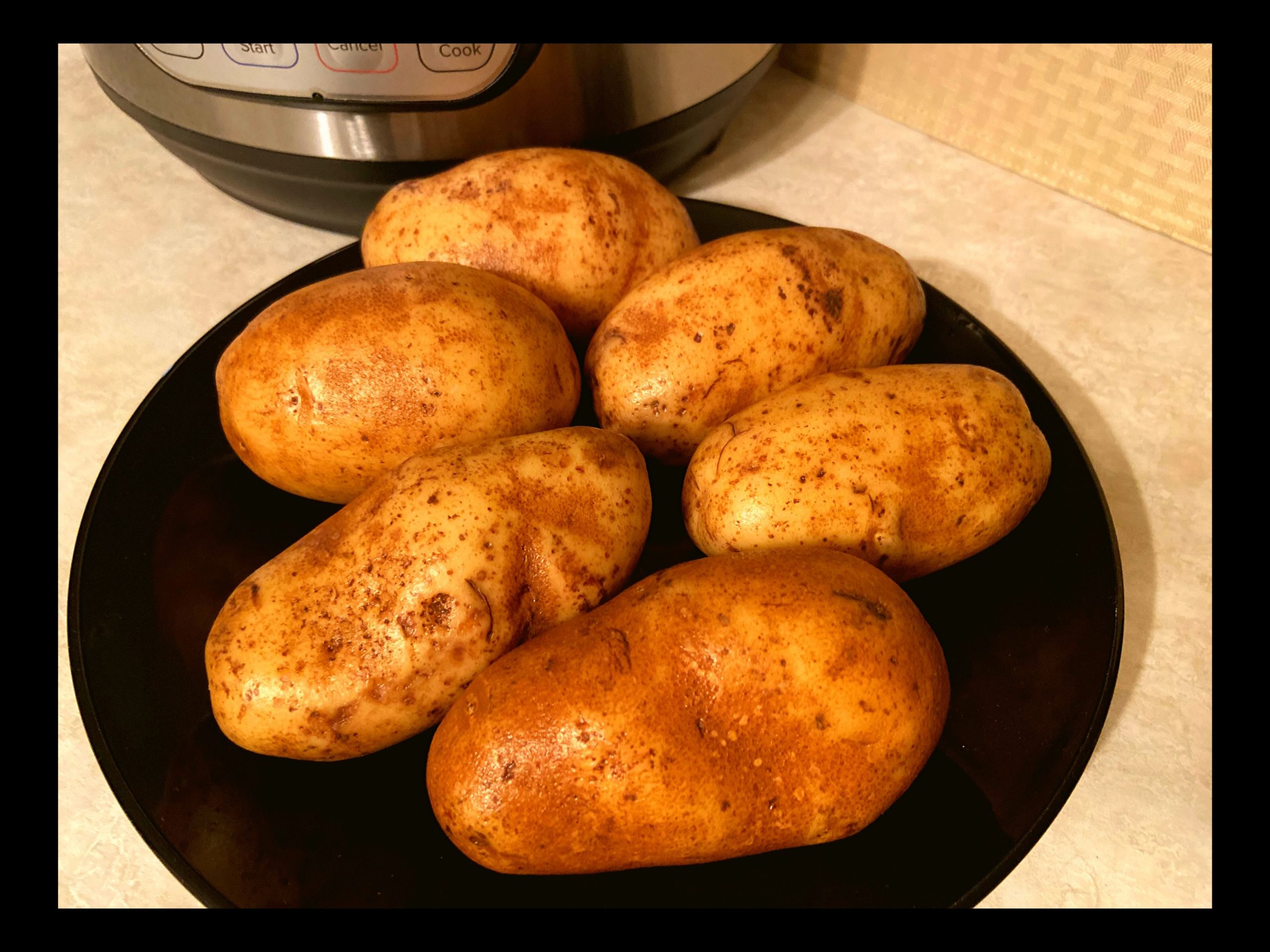Washed and scrubbed raw potatoes on a black plate in front of an Instant Pot.