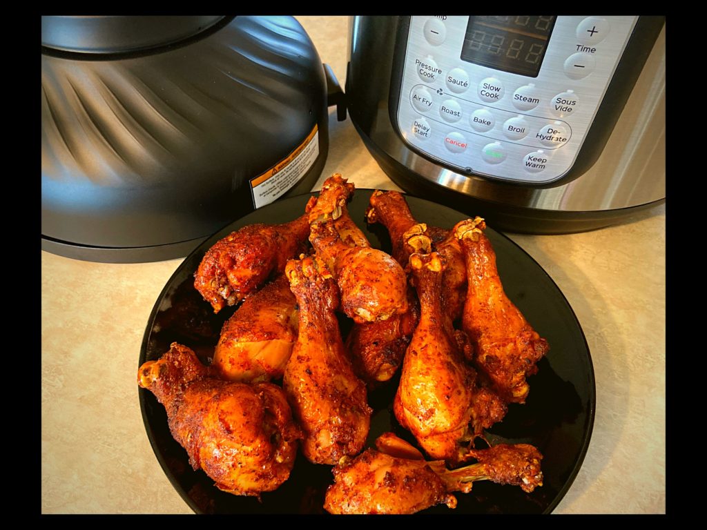 A black plate with BBQ chicken Drumsticks, Instant Pot, and Instant Pot air fryer lid all sitting on top of a kitchen counter