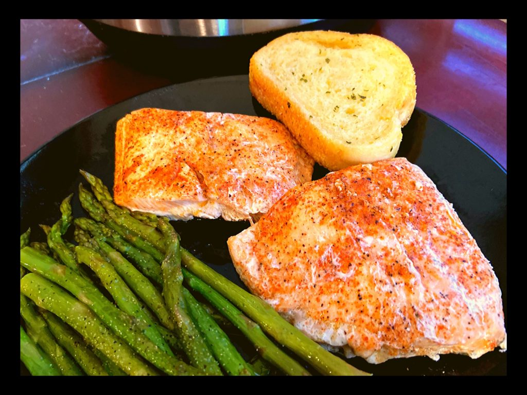 A black plate with seasoned and cooked salmon and asparagus next to an Instant Pot.