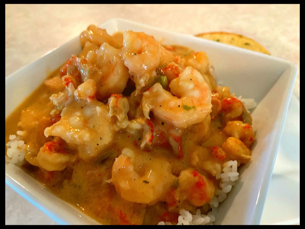 A white bowl filled with white rice topped with shrimp and crawfish etouffee and a garlic bread.