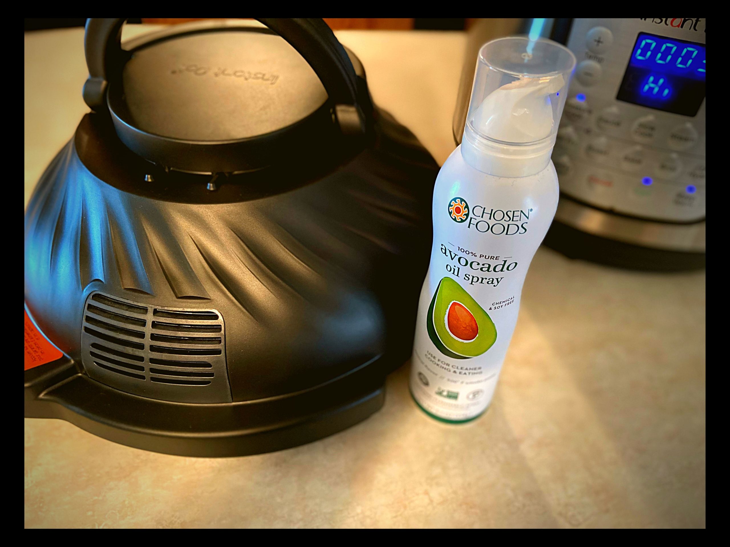 An Instant Pot Duo Crisp plus air fryer and a bottle of Avocado oil spray sitting on a kitchen counter top.