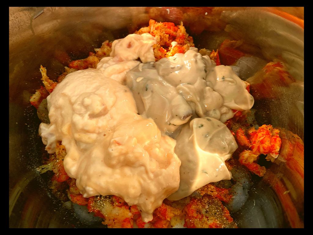 An instant pot filled with shrimp and crawfish tails topped with seasoning, a can of cream of mushroom and a can of cream of shrimp not stirred.