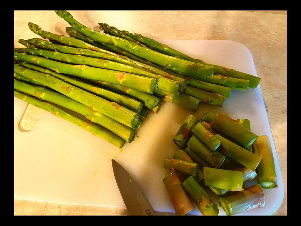 Asparagus on a cutting board with the ends cut off laying next to a knife.