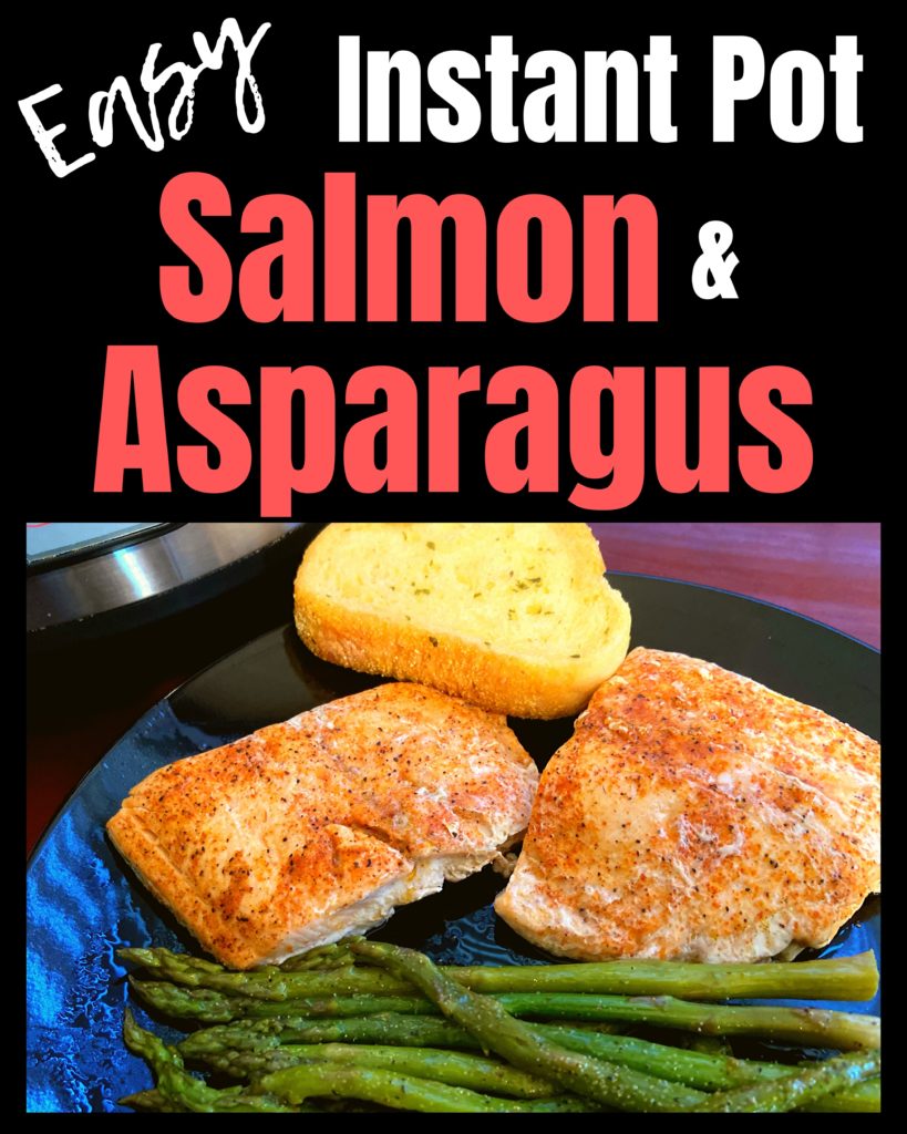 A black plate with seasoned and cooked salmon, asparagus, and a garlic bread sitting on a table top in front of an Instant Pot.