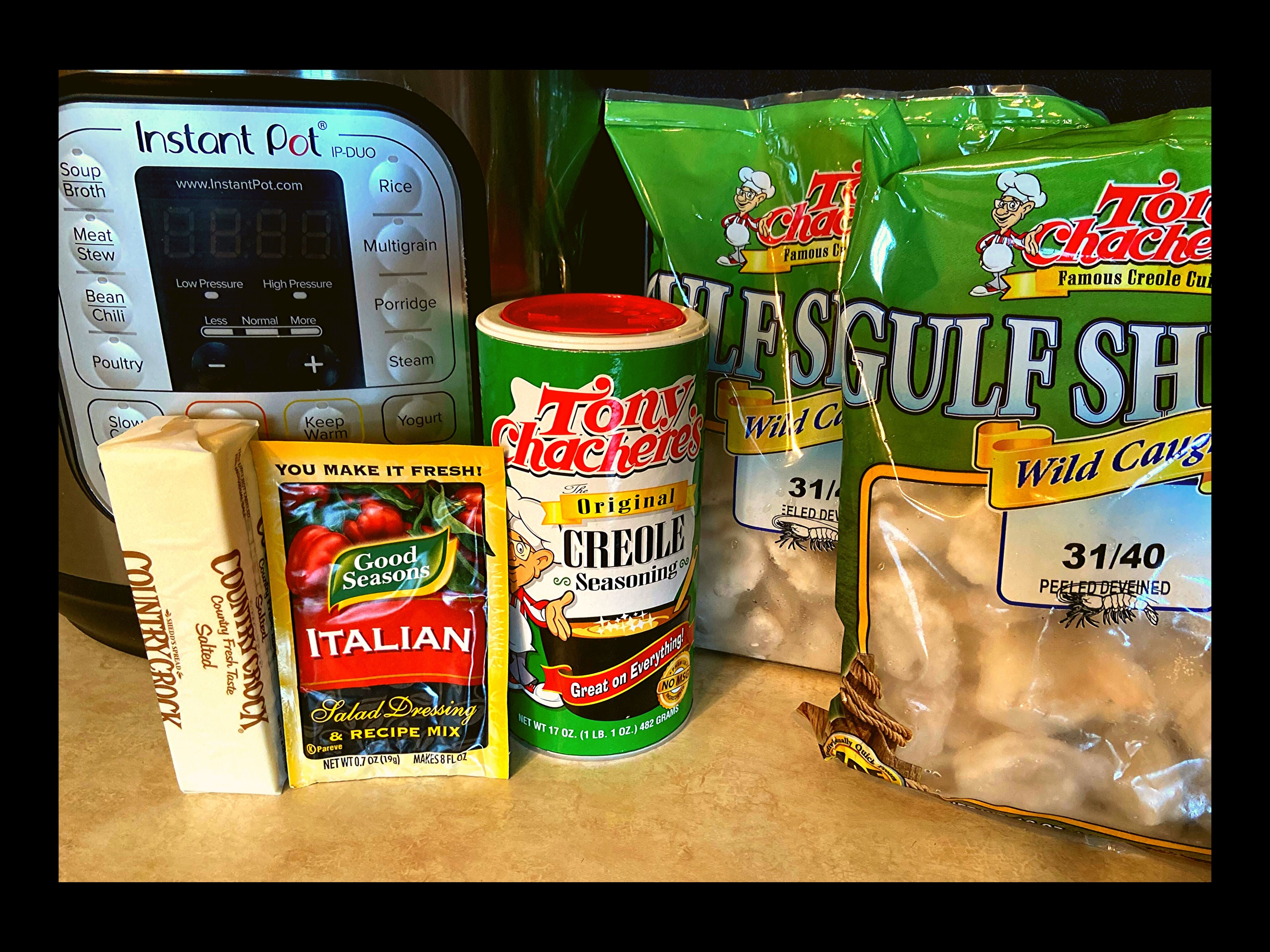 An Instant Pot, tony chachere's seasoning, Italian Seasoning Mix (powder), stick of butter, and 2 pounds of raw shrimp sitting on a kitchen counter.