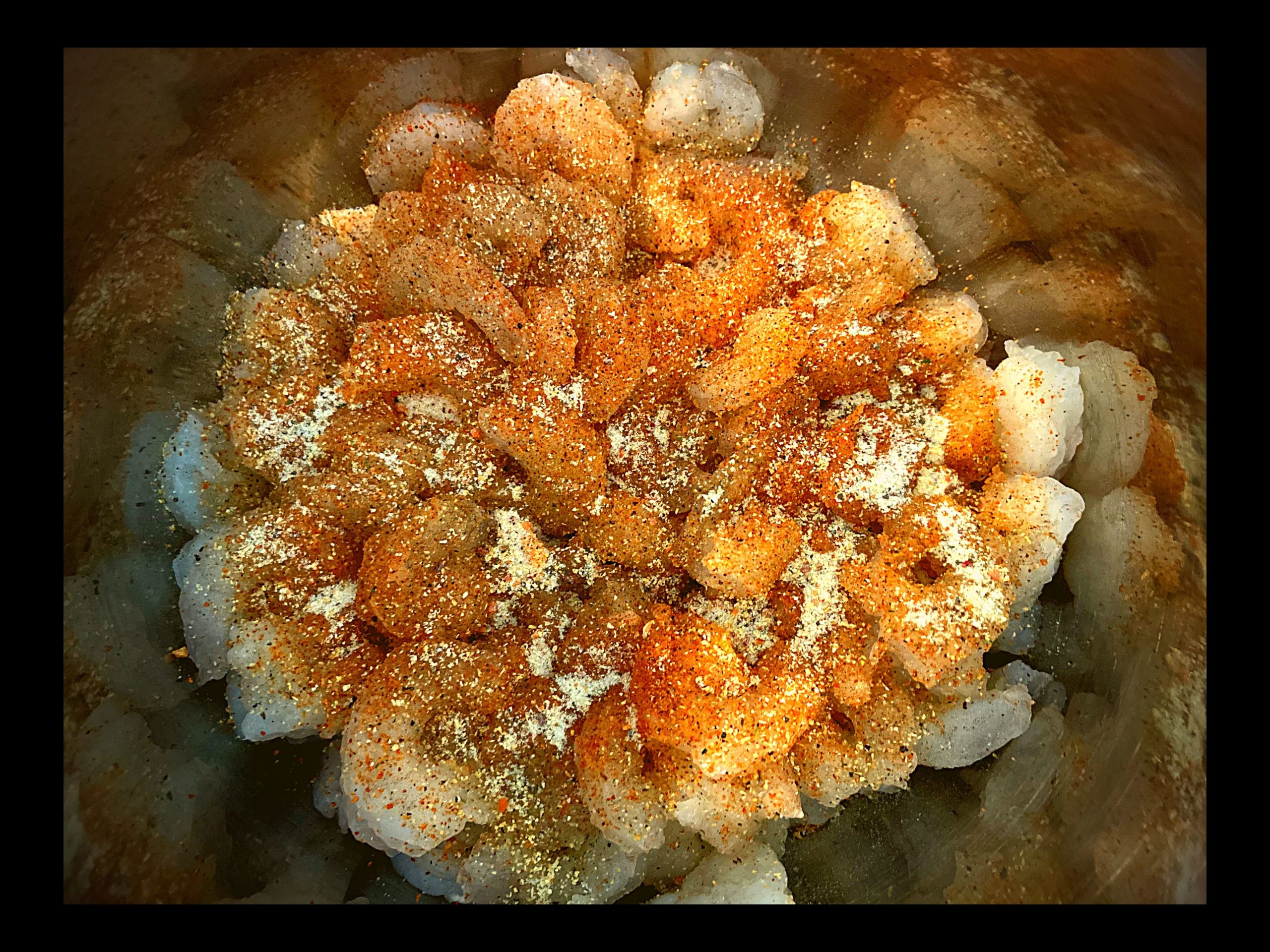 The inside of an Instant Pot filled with butter, raw shrimp, Italian powder seasoning and Tony Chachere's.