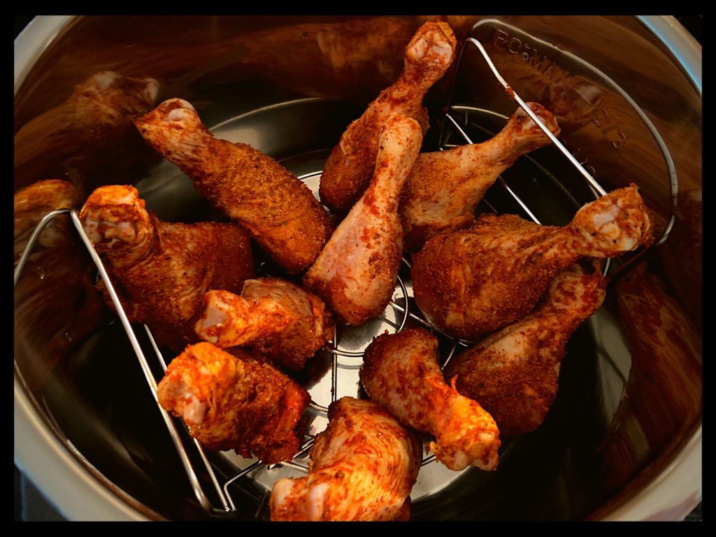 The inside of an Instant Pot filled with raw chicken legs on a trivet.