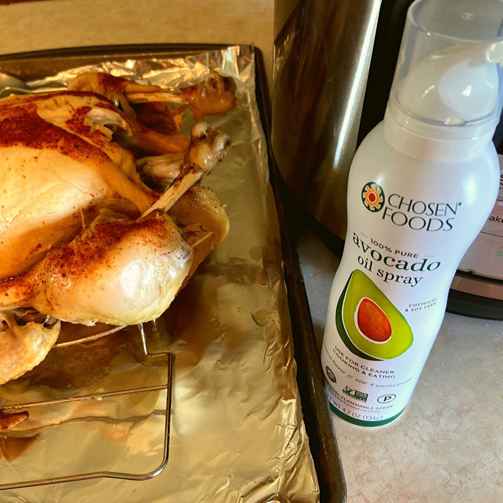 A bottle of avocado oil spray next to a Instant Pot and a tray with a pressure cooked chicken on it.